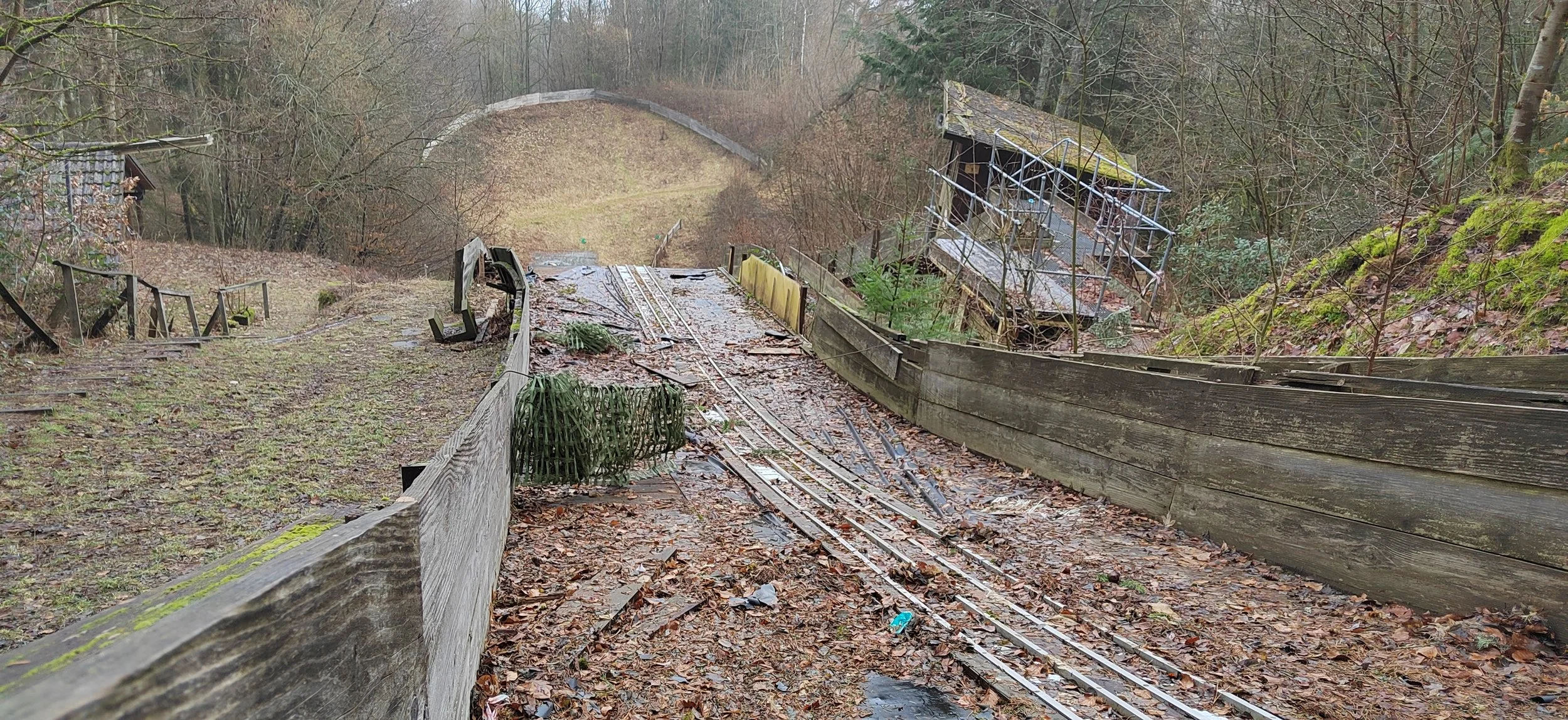 Burgtreppen rechts und links mit Laub bedeckt, zerbrochene Eisenbahnschienen in der Mitte, abgebrochene Holzbarrieren, verfallene Gebäude im Hintergrund, umgeben von Bäumen im Herbst.