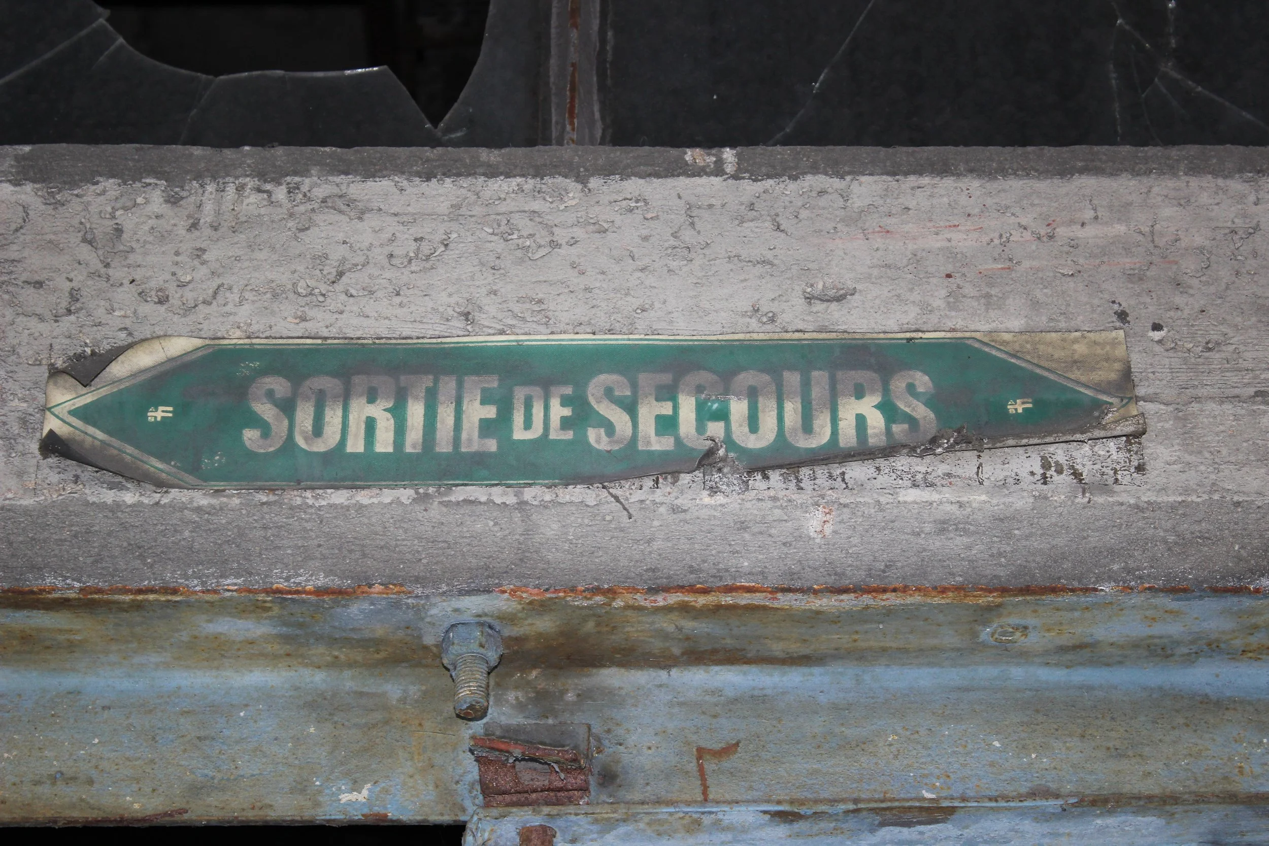 Ein alter, beschädigter grüner Rettungsschild mit der Aufschrift 'SORTIE DE SECOURS'.