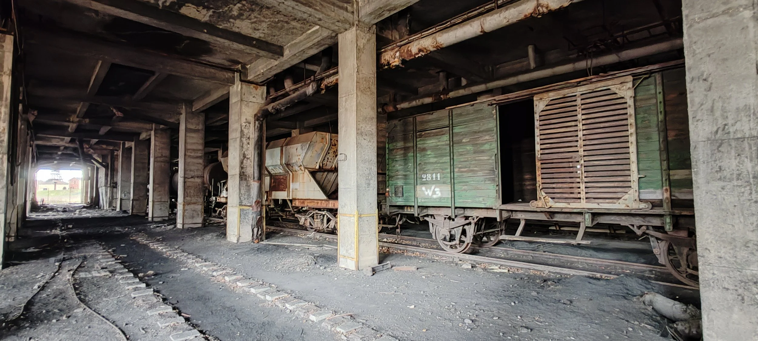 Altlasten im Tunnel, mit alten, verrosteten Eisenbahnwagen und zerbrochenen Gleisen, Staub und dunkler Atmosphäre.