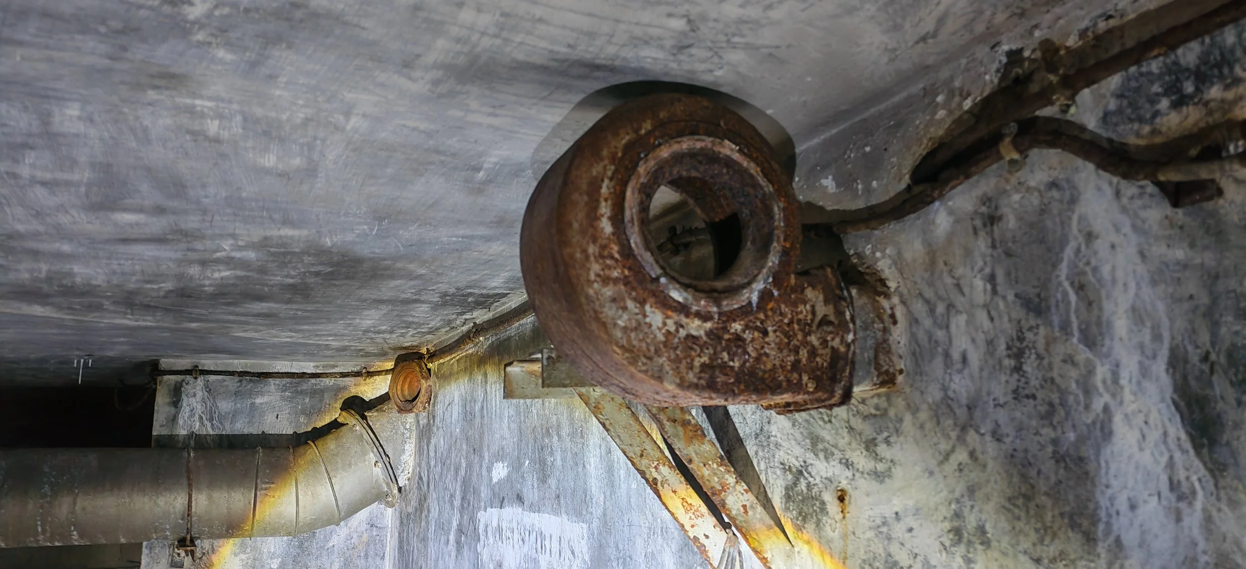 Rostige Metallröhre in einer alten Fabrikumgebung, teilweise mit rostigem Staub bedeckt, auf einer Steinfäche liegend.