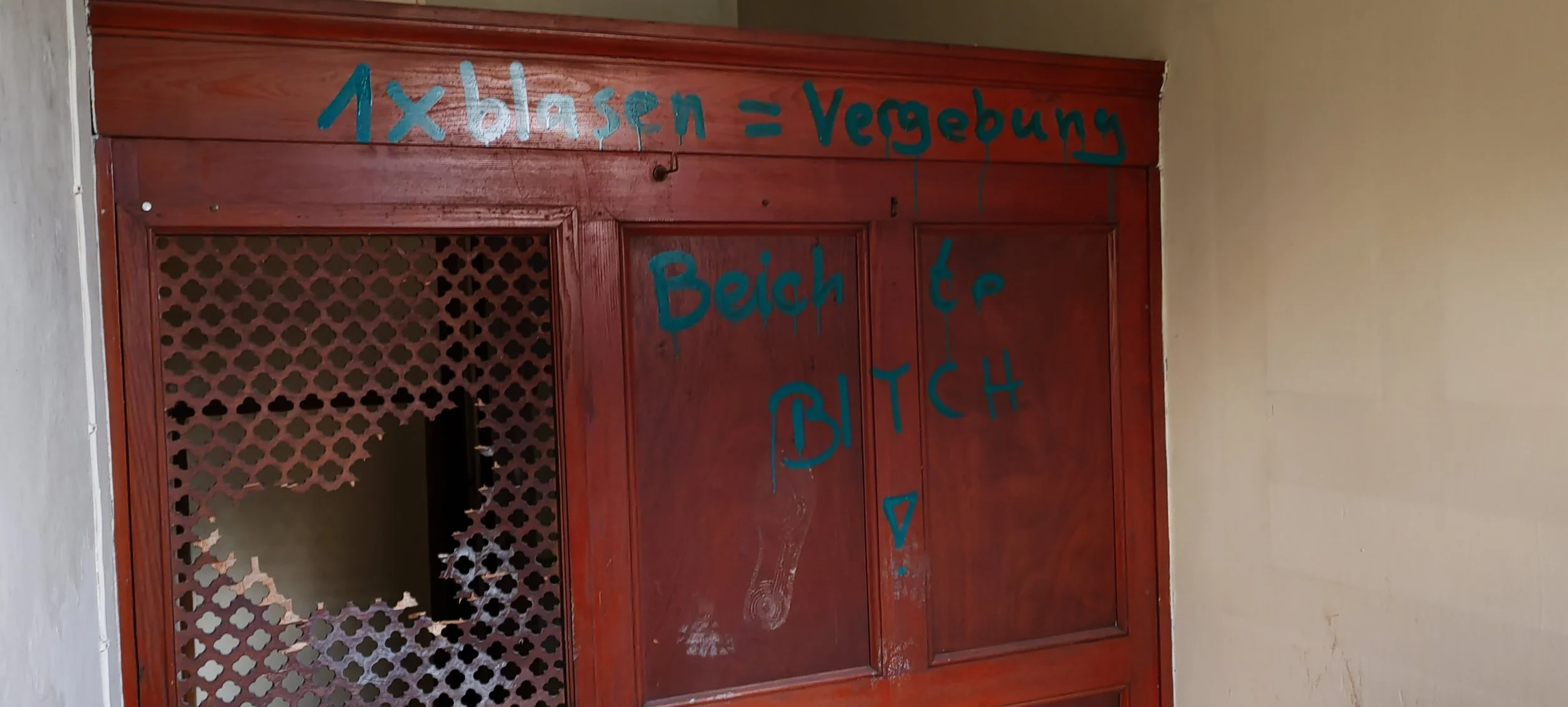 Ziegelmauer mit Holzrahmen, auf dem in blauer Schrift steht: '1 x blasen = Vergabeung', 'Beicht' und andere kaum lesbare Wörter.