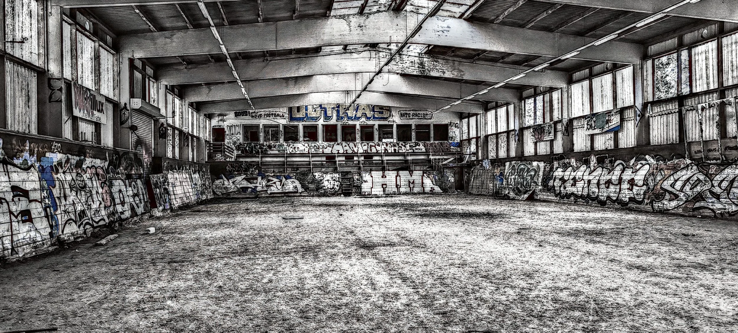 Verlassener, verstaubter Indoor-Fußballplatz mit Graffiti an den Wänden, durch die schmutzigen Fenster fällt Licht auf den Boden