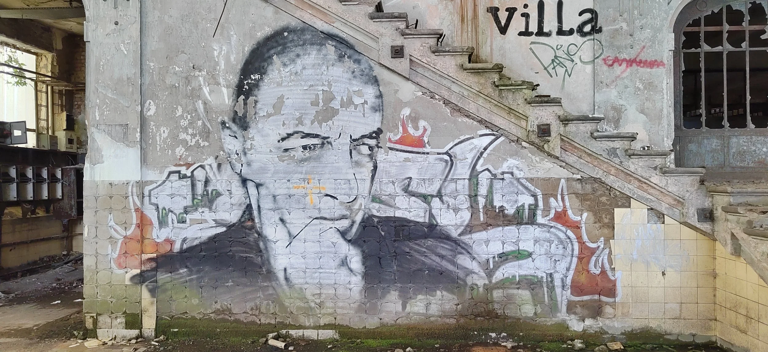 Graffiti eines Mannes auf einer alten, verfallenen Wand mit Treppe, in einer verfallenen, urbanen Umgebung.