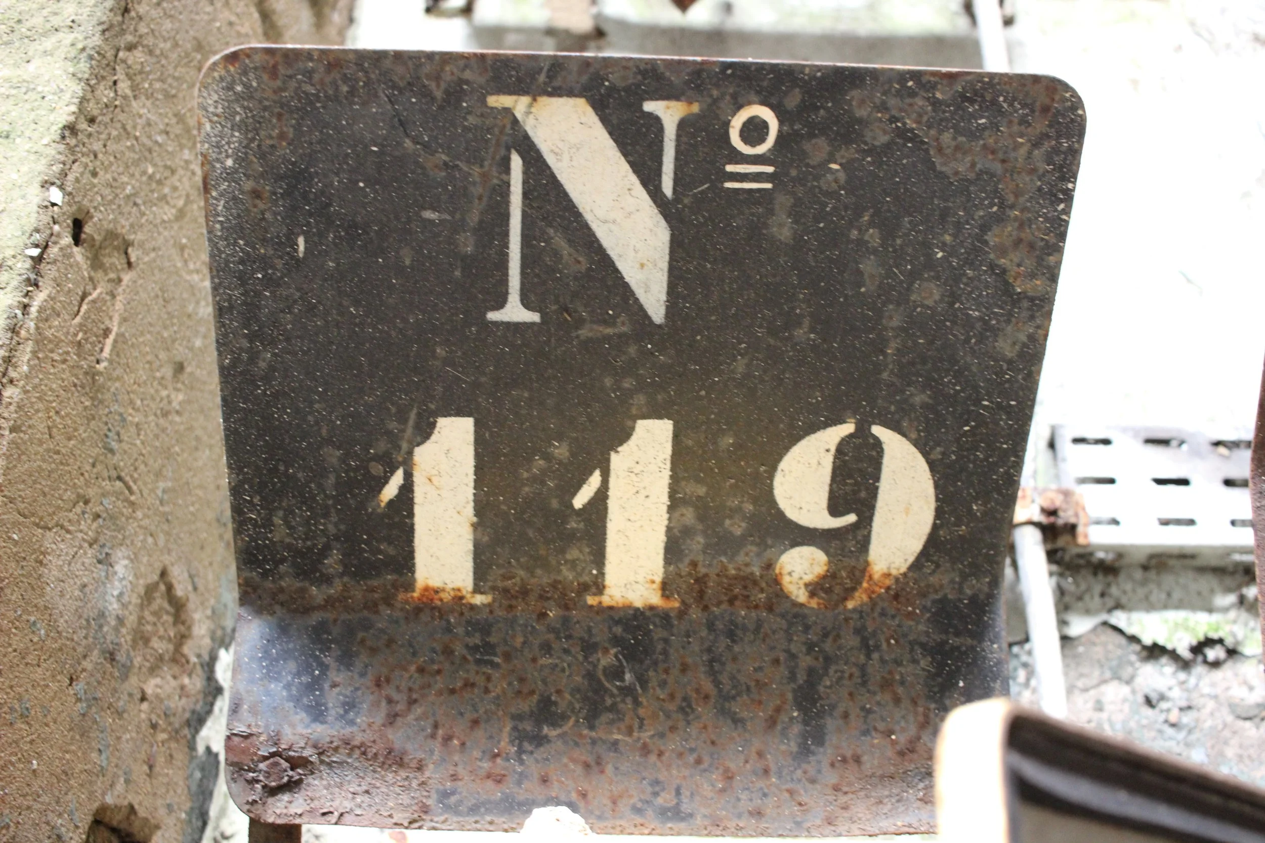 Alte, rostige Metalltafel mit der Nummer 119 und dem Zeichen 0º, befestigt an einer Mauer.