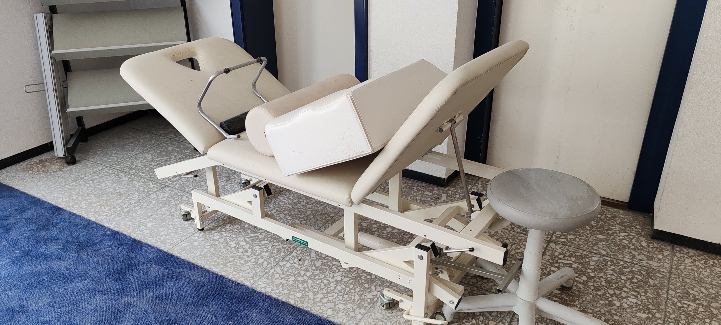 Alter medizinischer Untersuchungsstuhl mit Liegefunktion und begleitendem Hocker in einer Klinik oder Praxisumgebung