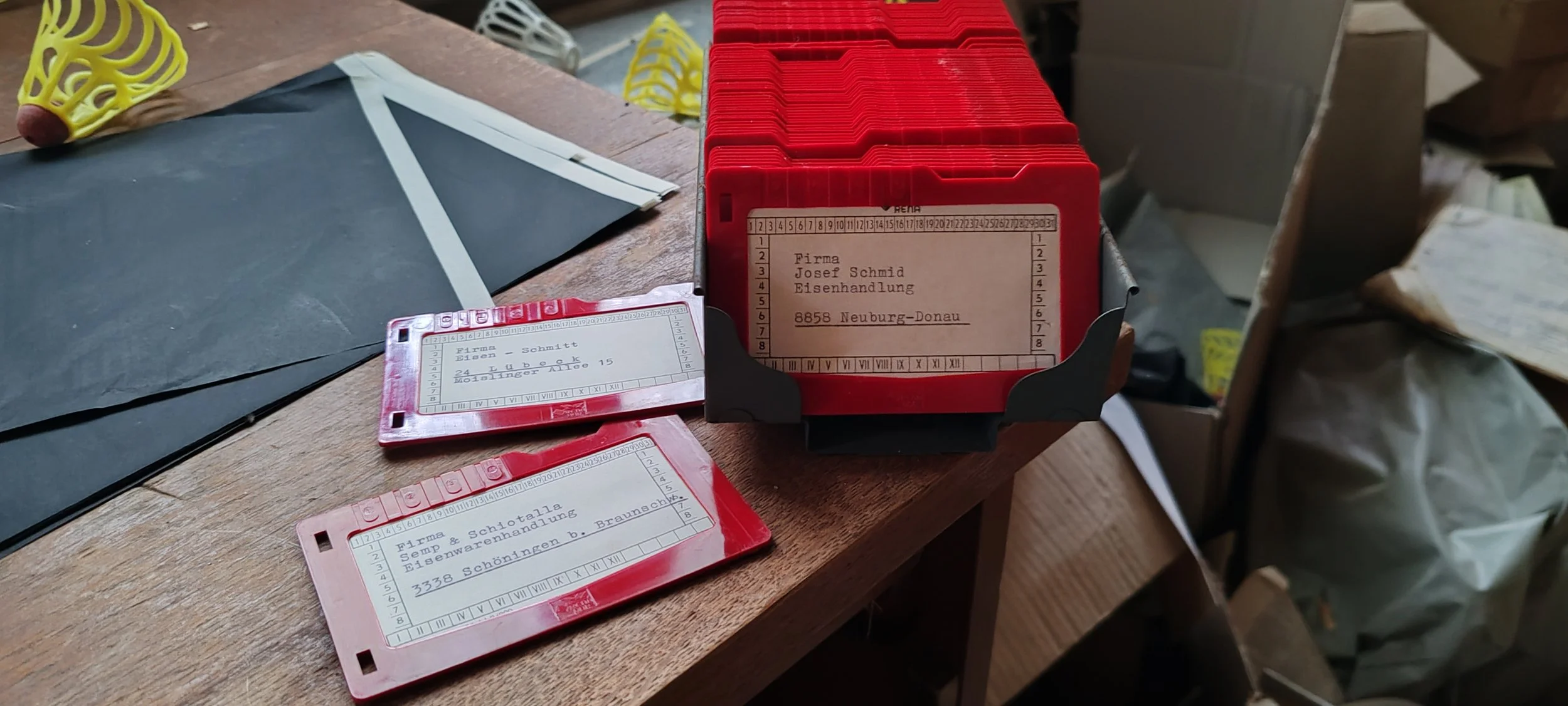 verschiedene rote und pinke Karten mit Wörtern und Adressen, die in einem schwarzen Kartenhalter sitzen, sowie schwarze und weiße Papiere und andere Gegenstände auf einem Holztisch