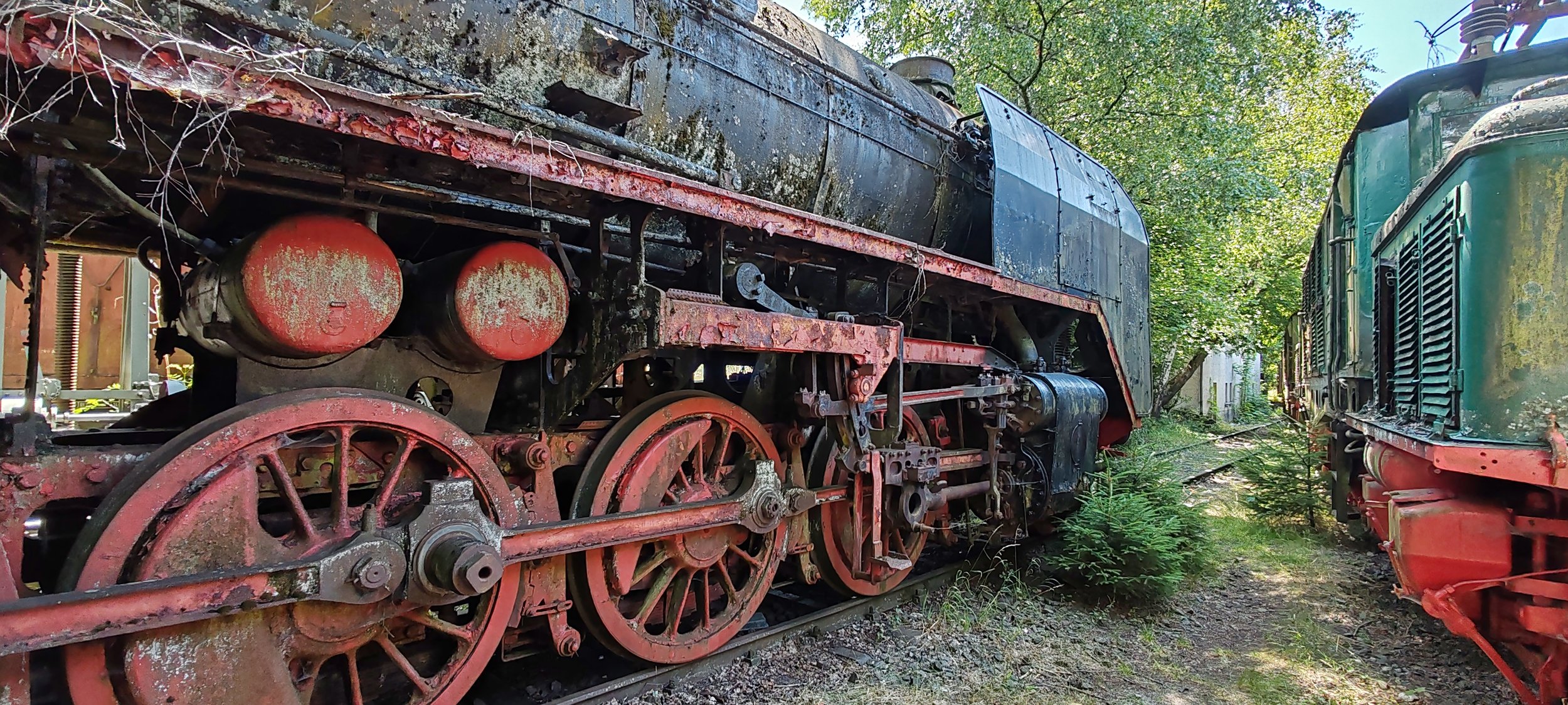 Ein alter verrosteter Güterzugwagen aus Metall, der auf einem Gleis steht, umgeben von Bäumen und Pflanzen.