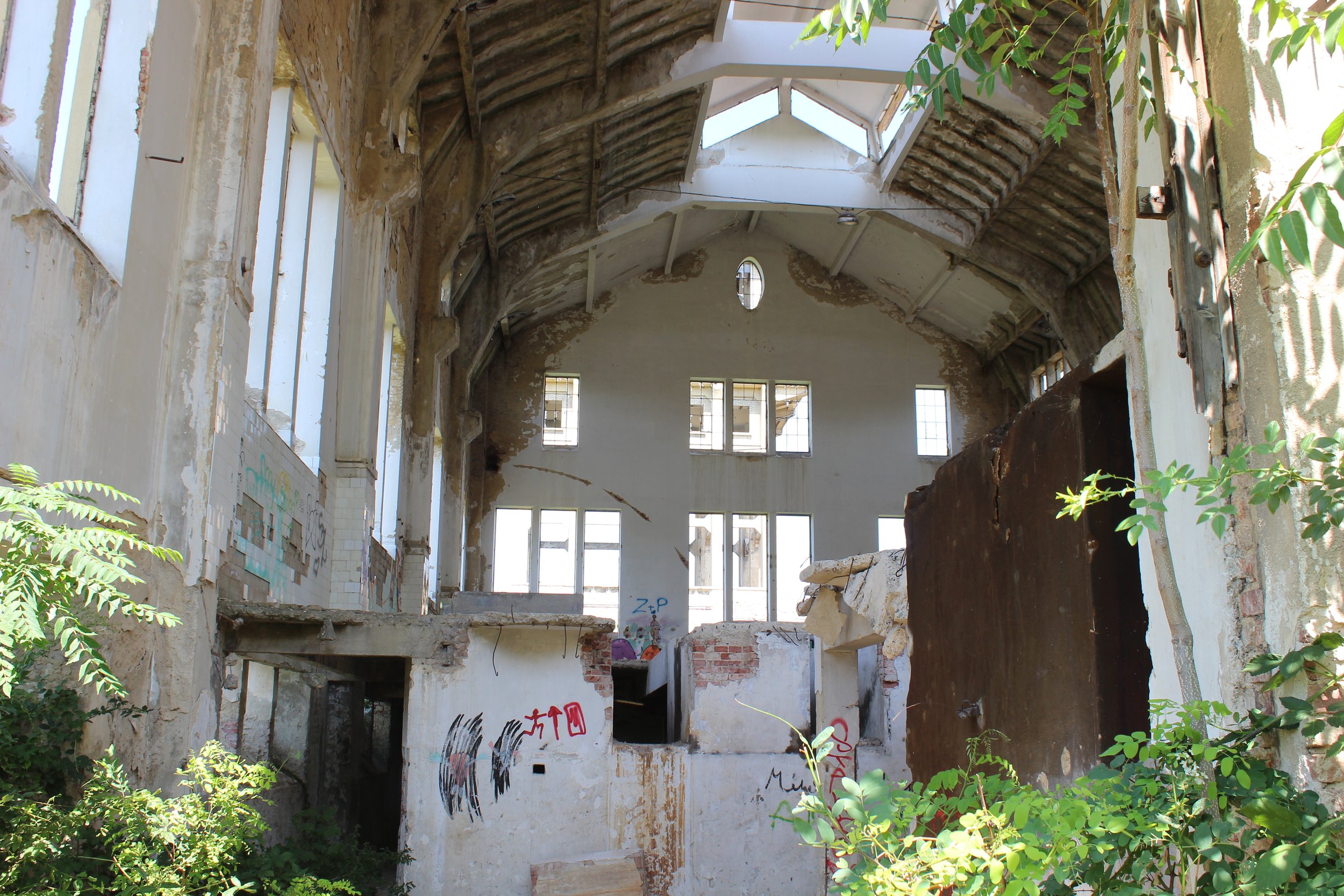 Verfallene, offene Kirche mit zerbrochenen Fenstern, beschädigtem Dach und Graffiti an den Wänden, umgeben von Pflanzen.