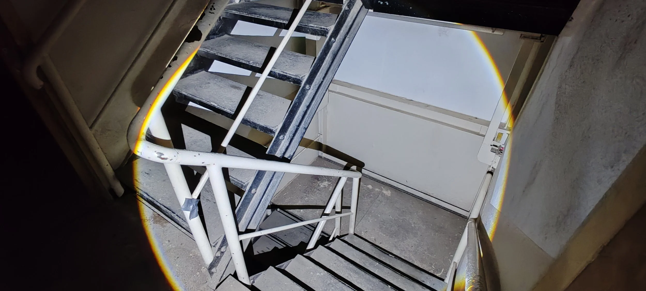 Innenaufnahme eines Gebäudes mit einer Metalltreppe und einem Abgrund, durch den eine Regenbogen sichtbar ist.