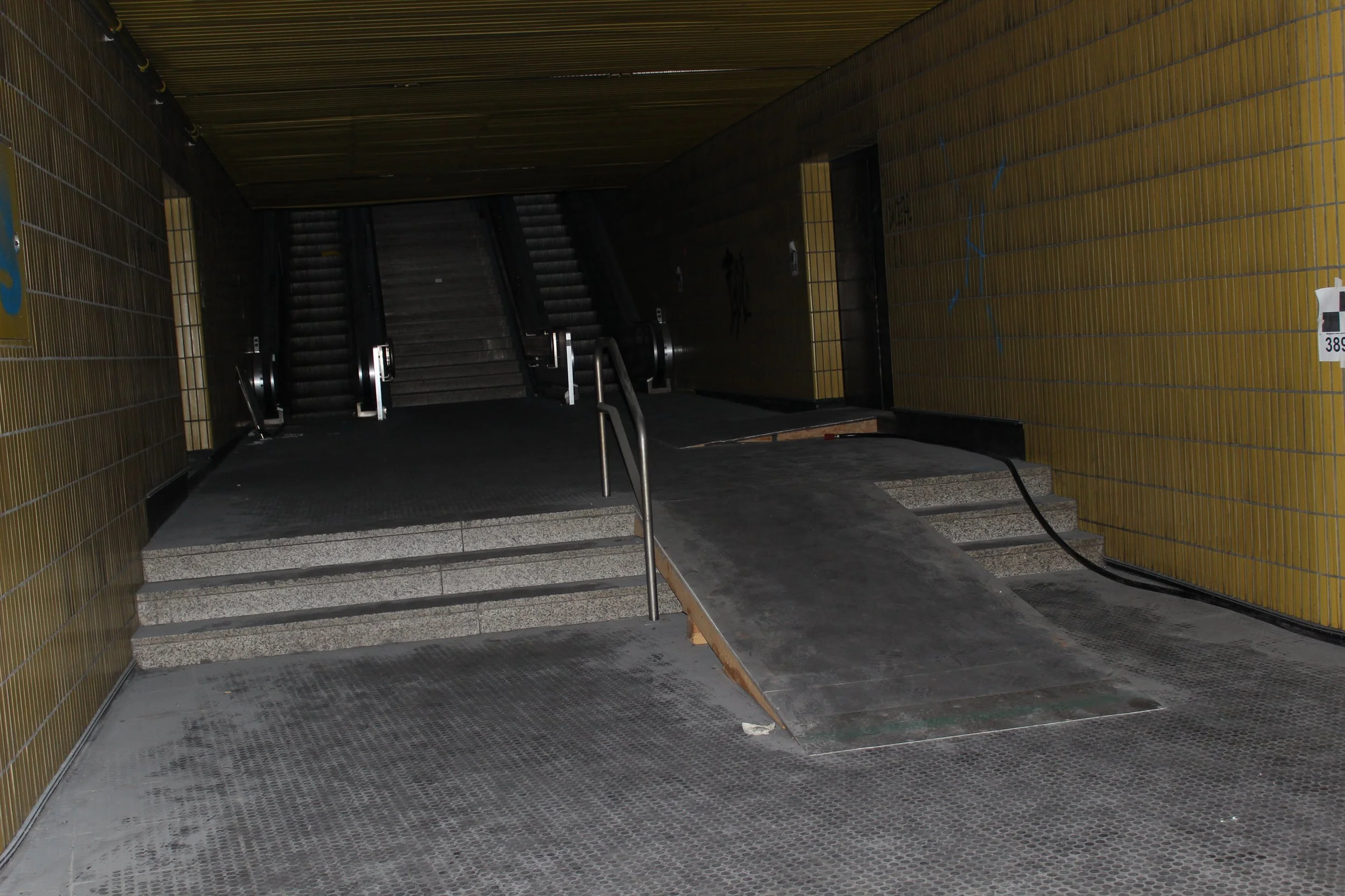 Eingang zu einer U-Bahn-Station mit Rollstuhlrampe, Treppen und Rolltreppen in einem dunklen Tunnel
