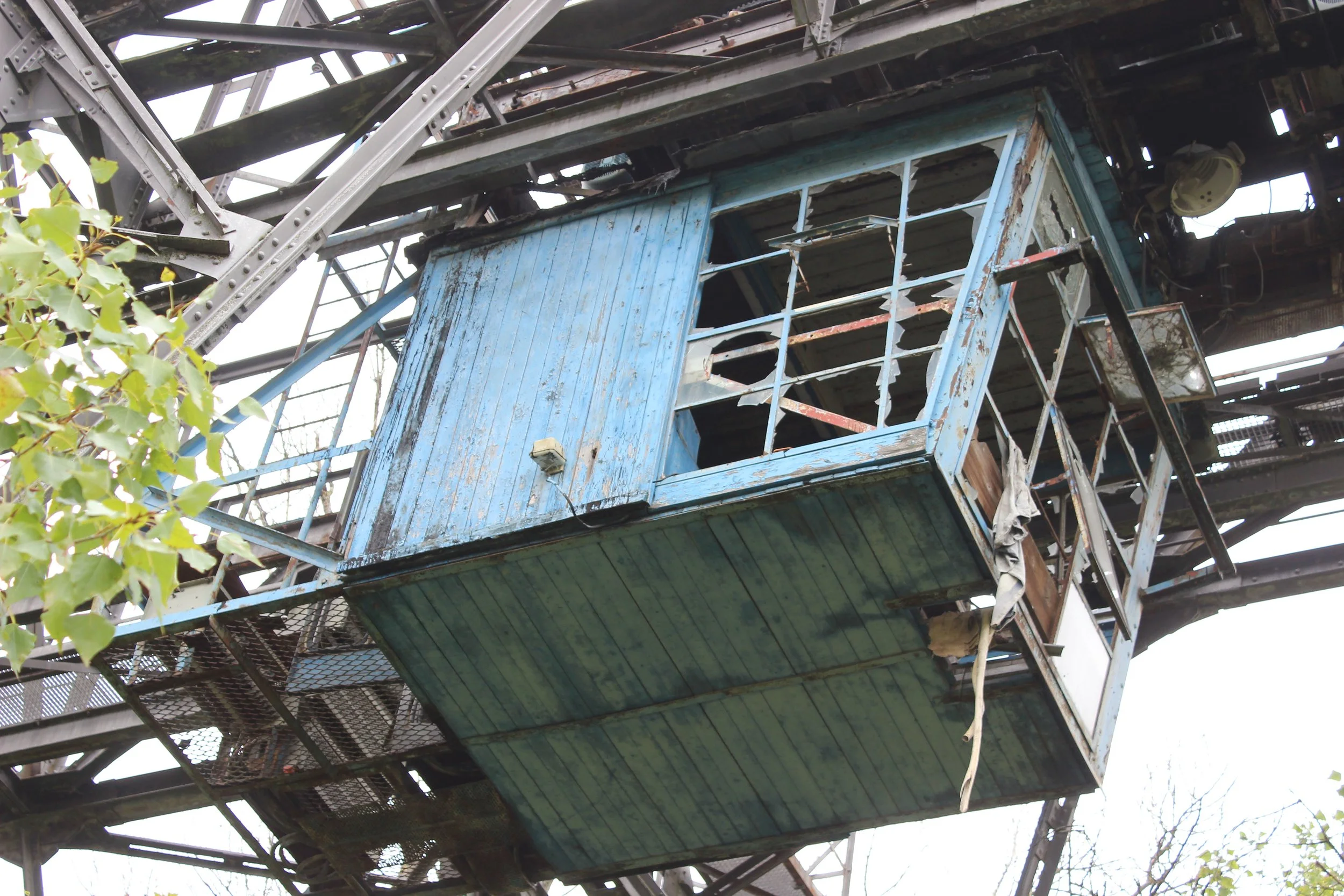 Verrosteter, blauer, verfallener Fahrkorb eines alten Riesenrads, das im Freien steht, mit sichtbaren Schäden und rostigen Metallteilen.