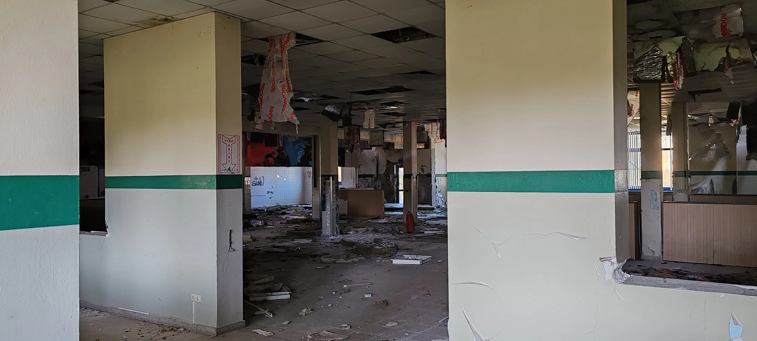 Innenaufnahme eines beschädigten und verfallenden Gebäudes, mit beschädigten Wänden, zerbrochenem Deckengebäude und herumliegenden Trümmern.