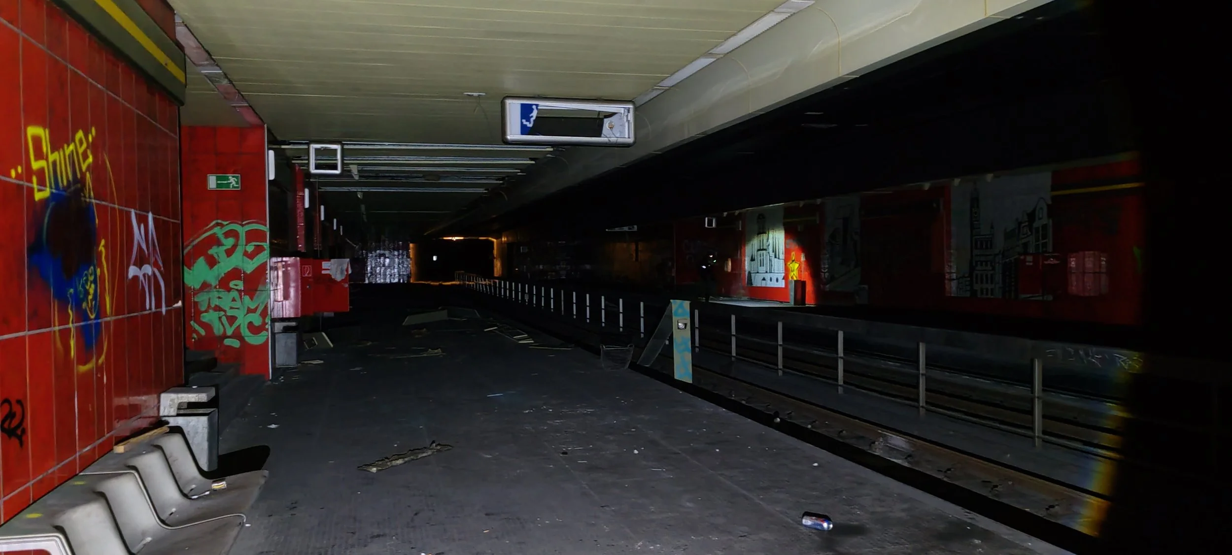 Verlassene U-Bahn-Station mit Graffiti auf den Wänden, dunkle Beleuchtung, abgestellte Sitzbänke, Müll auf dem Boden, in der Nähe des Gleises.