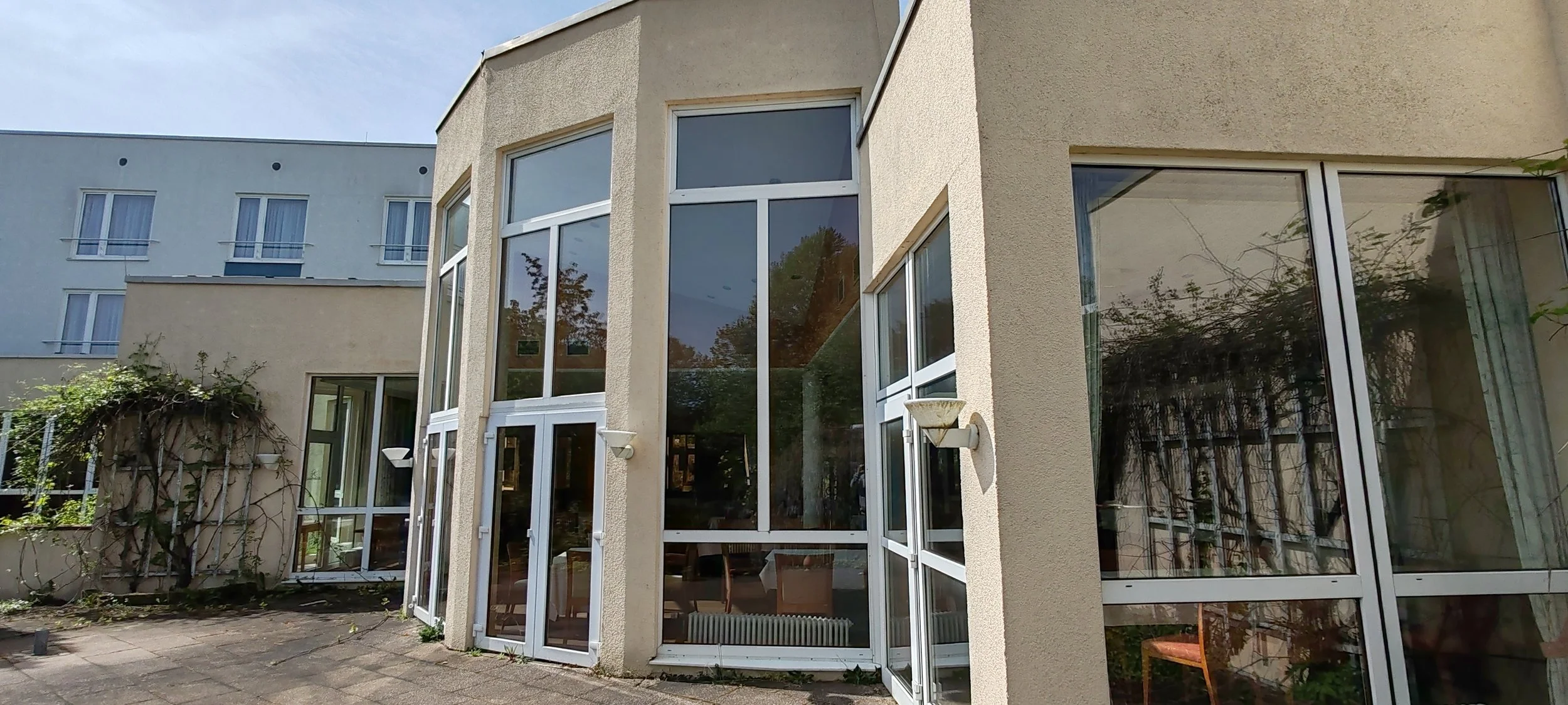 Modernes Gebäude mit großen Fensterflächen und einem gepflegten Außenbereich, teilweise bewachsen mit Kletterpflanzen.