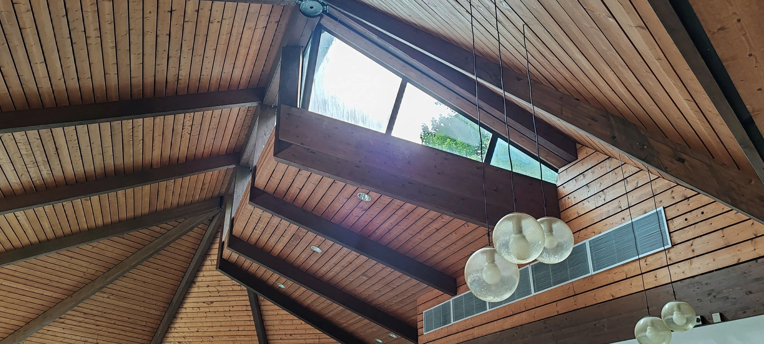 Holzverkleidung und Dachfenster im Innenraum eines Gebäudes mit modernen Beleuchtungsleuchten.