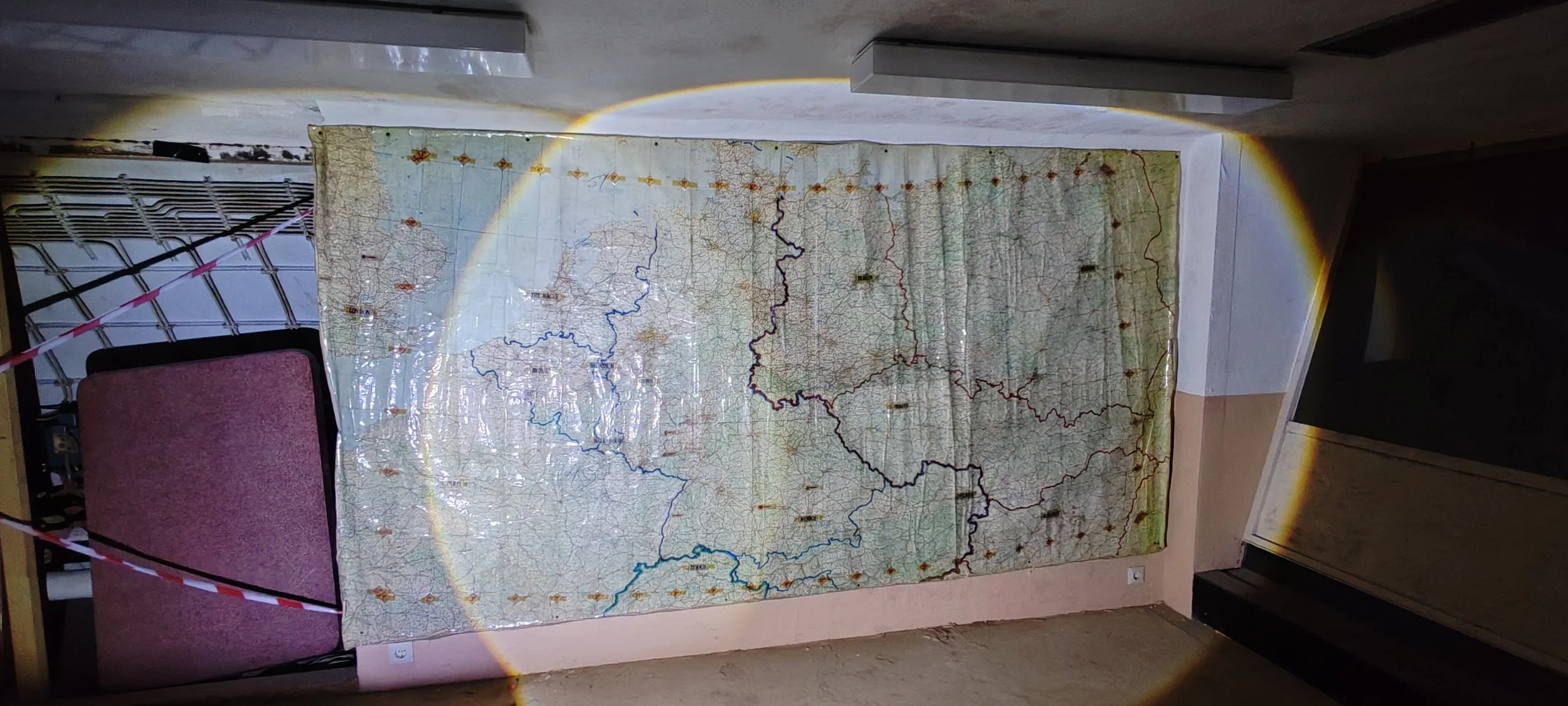 Ein alter, großer, gefalteter Stadtplan hängt an einer Wand, beleuchtet vom Sonnenlicht, mit sichtbaren Rissen und Gebrauchsspuren.