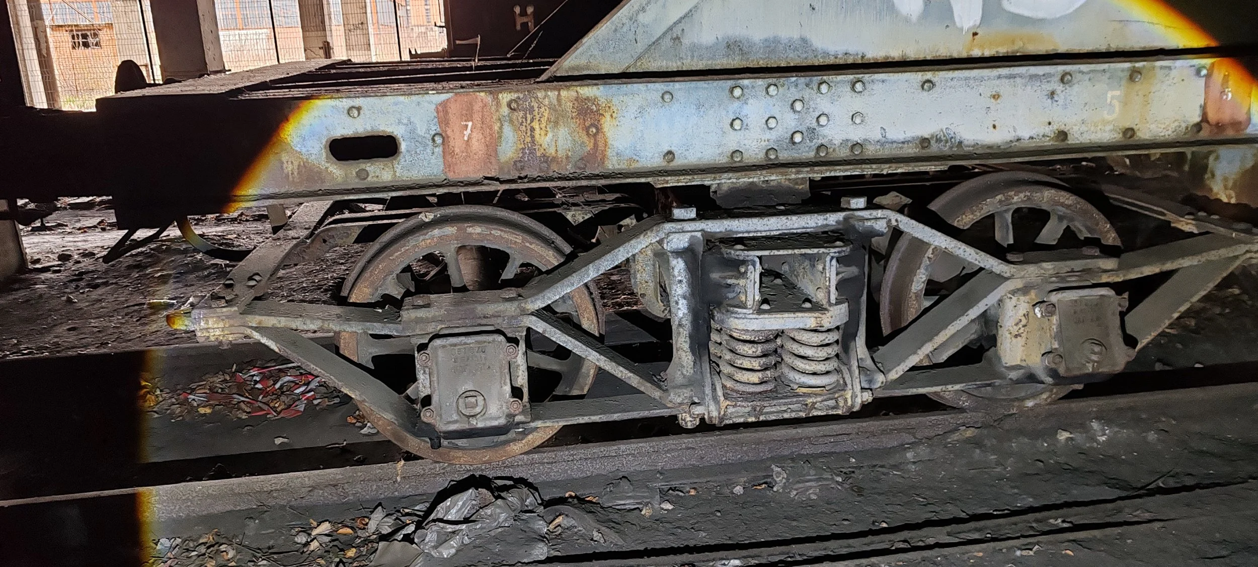 Nahaufnahme eines alten, rostigen Eisenbahnwagens mit sichtbaren Rädern, Federung und metallischer Struktur auf einem Gleis.