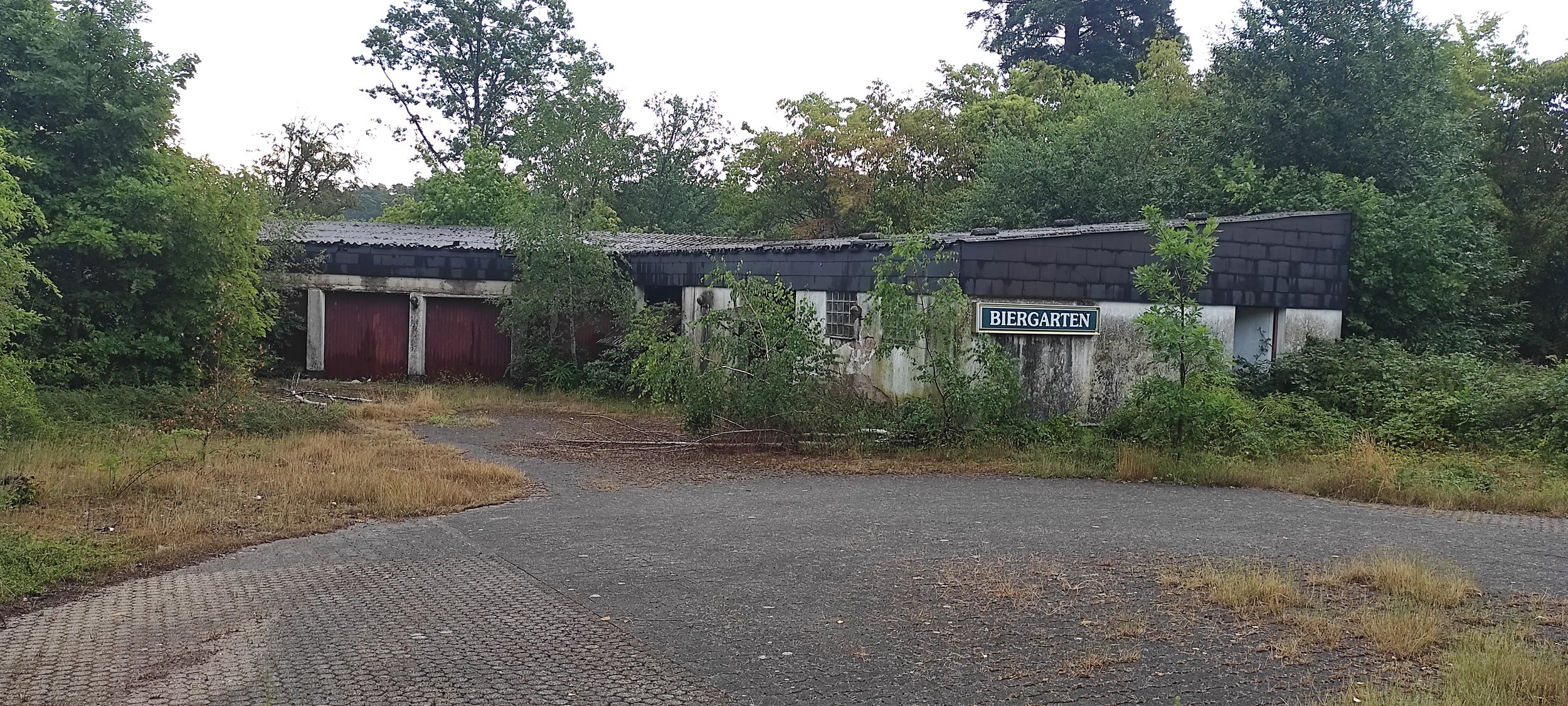 Verfallene Gebäude im Grünen mit einem Schild, das 'Biergarten' sagt.