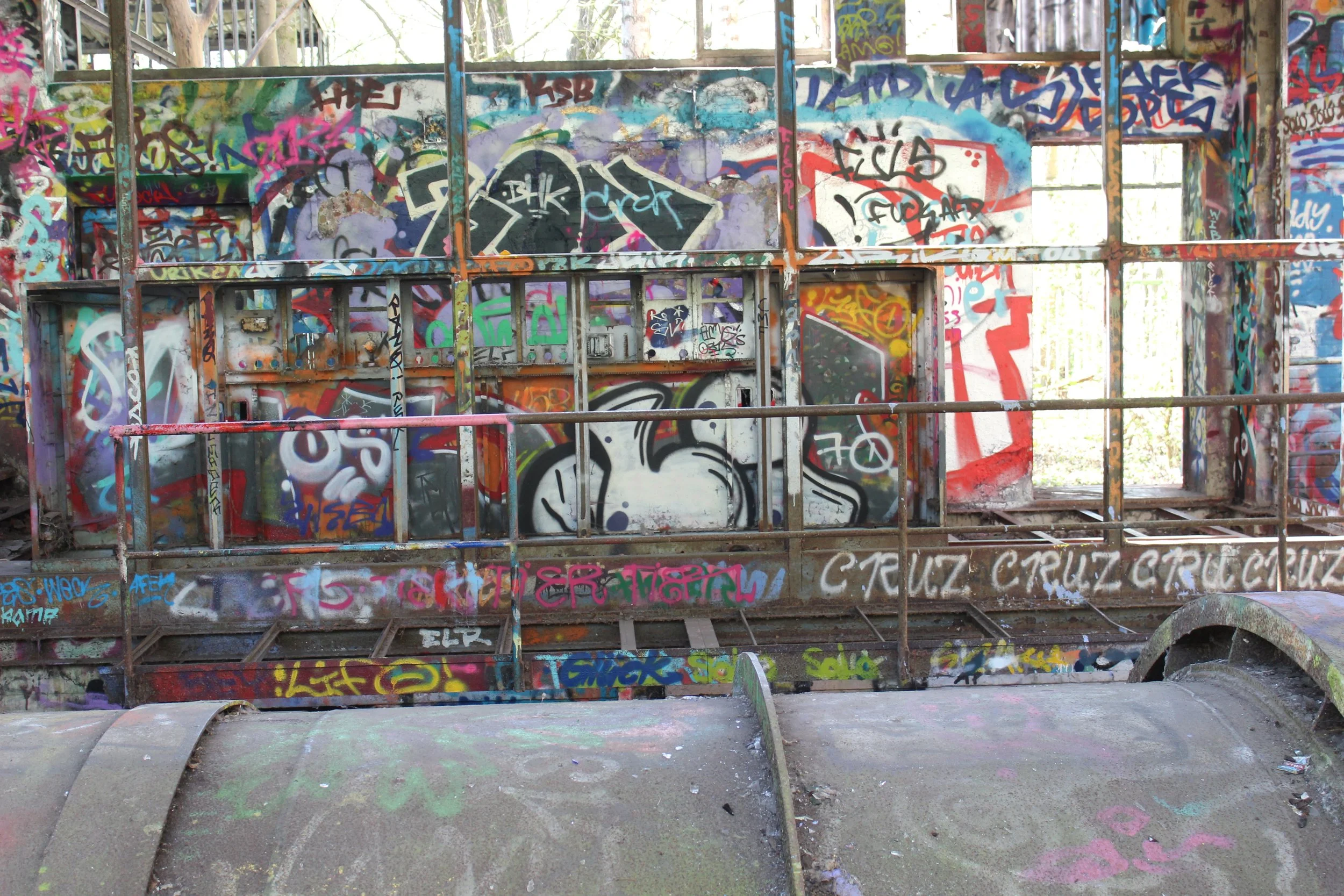 Graffiti bedeckter, verlassener Spielplatz mit rostigem Metall und bunten Wandkunst im Hintergrund.