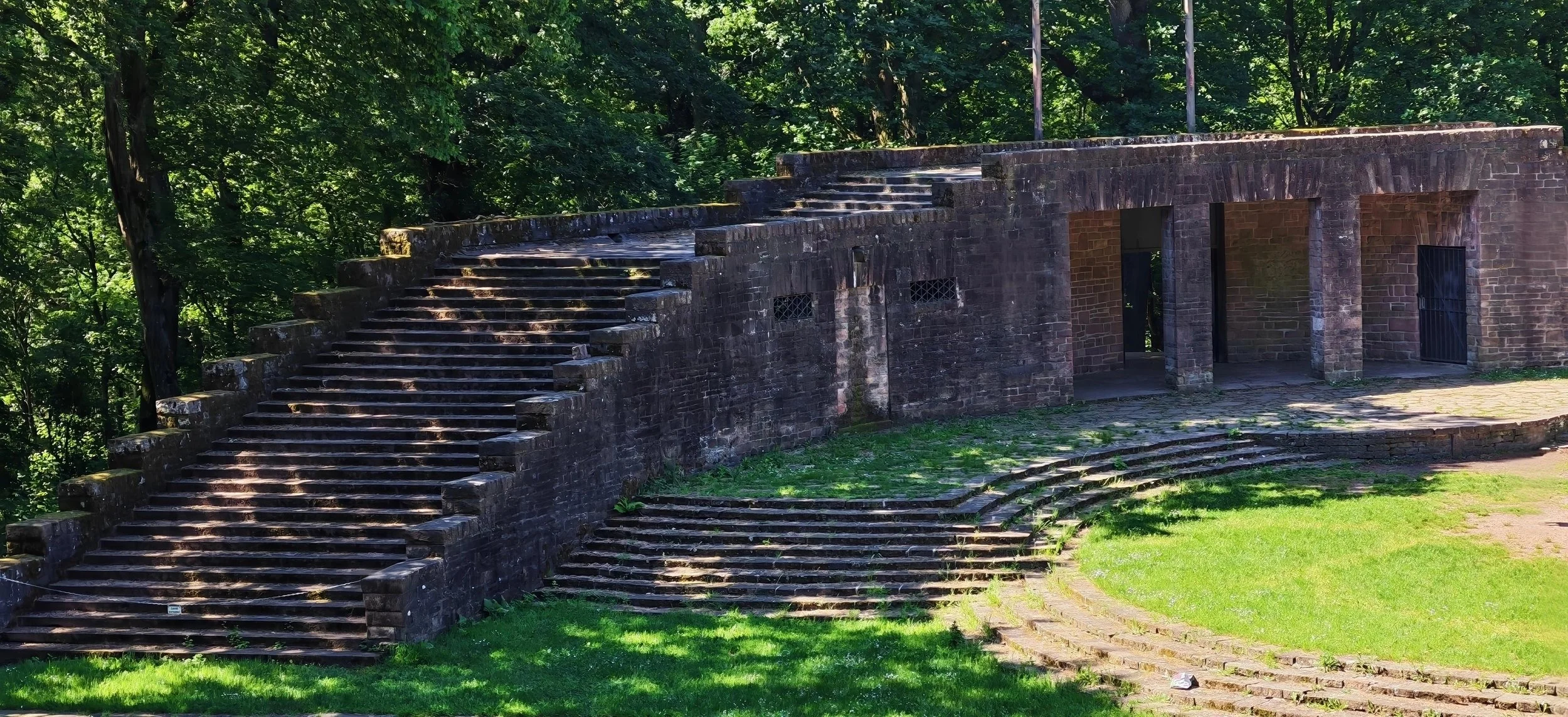 Steinerne Treppe und Überdachung, umgeben von grünen Bäumen im Park.