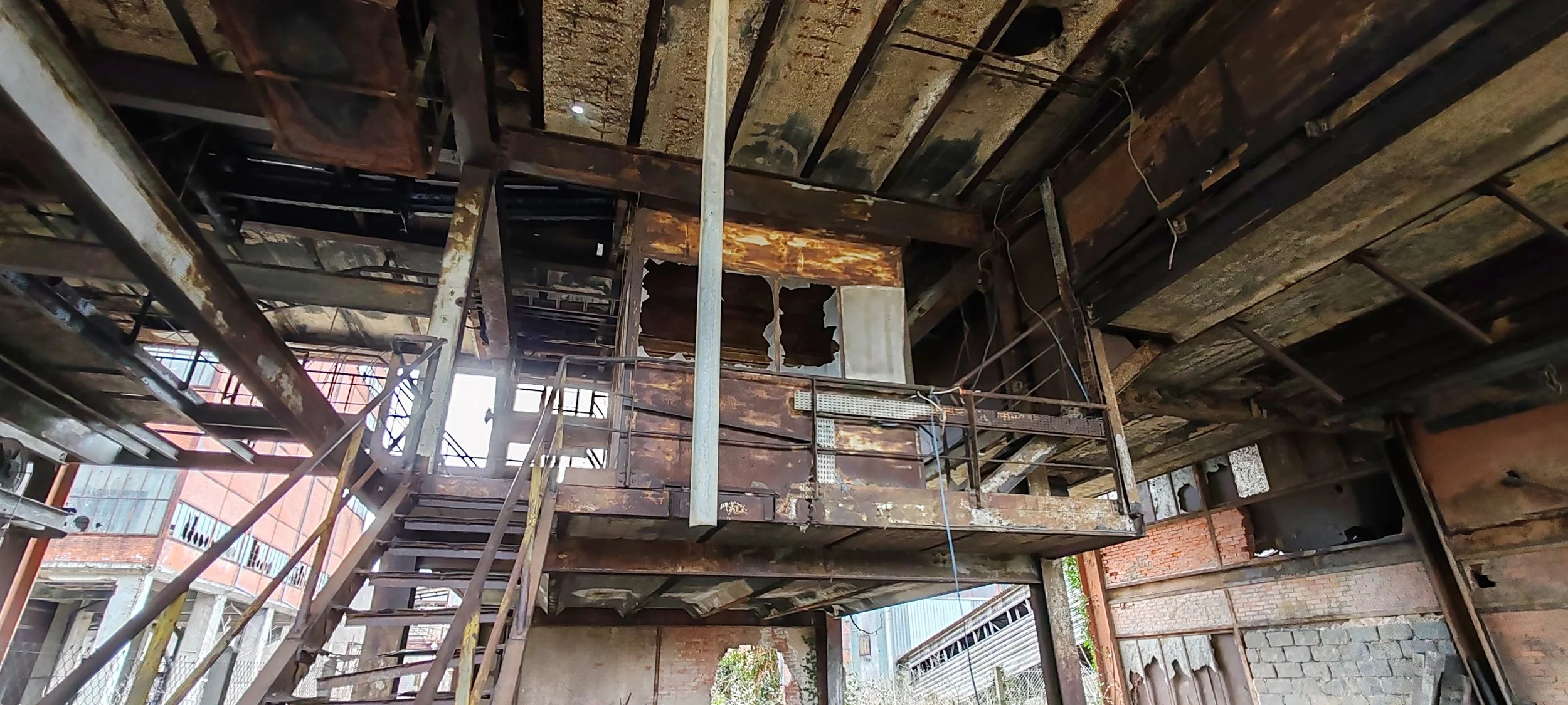 Das Bild zeigt eine veraltete, beschädigte loftartige Innenraumstruktur mit rostigem Metall, Holz und zerstörten Wänden.