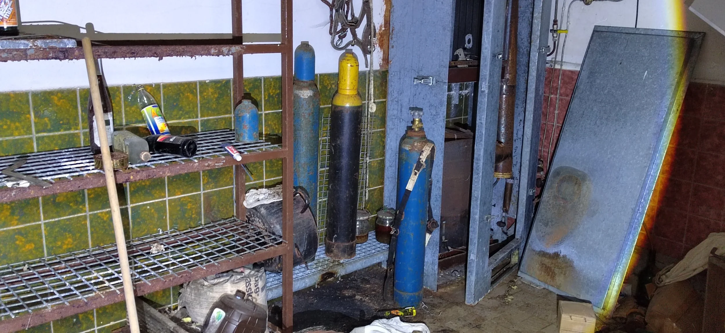 Verrostete Gasflaschen und Schränke in einem chaotischen Raum mit Schutt und Werkzeugen.
