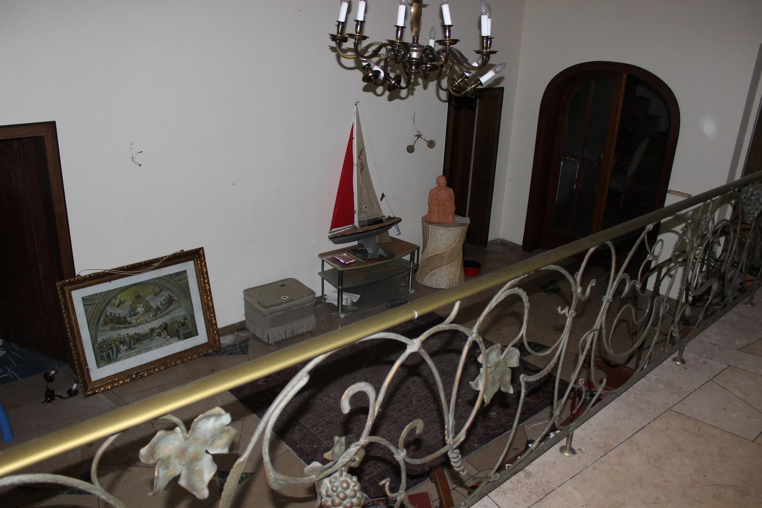 Innenraum eines Wohnzimmers mit antiker Dekoration, darunter ein Gemälde, eine Schiffmodell, Skulpturen, ein industrielles Regal, ein Teppich und ein Kronleuchter.