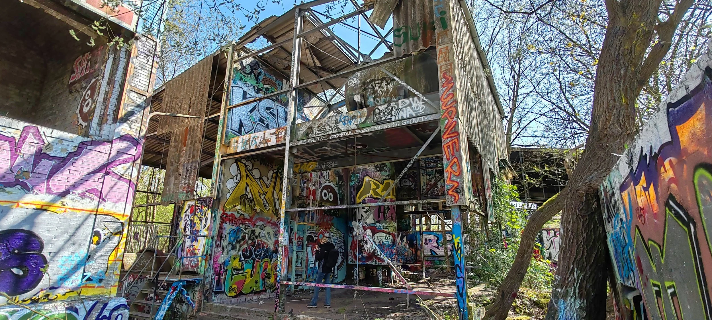 Verfallene, mit Graffiti bedeckte Gebäude und Wandflächen im Freien, umgeben von Bäumen.