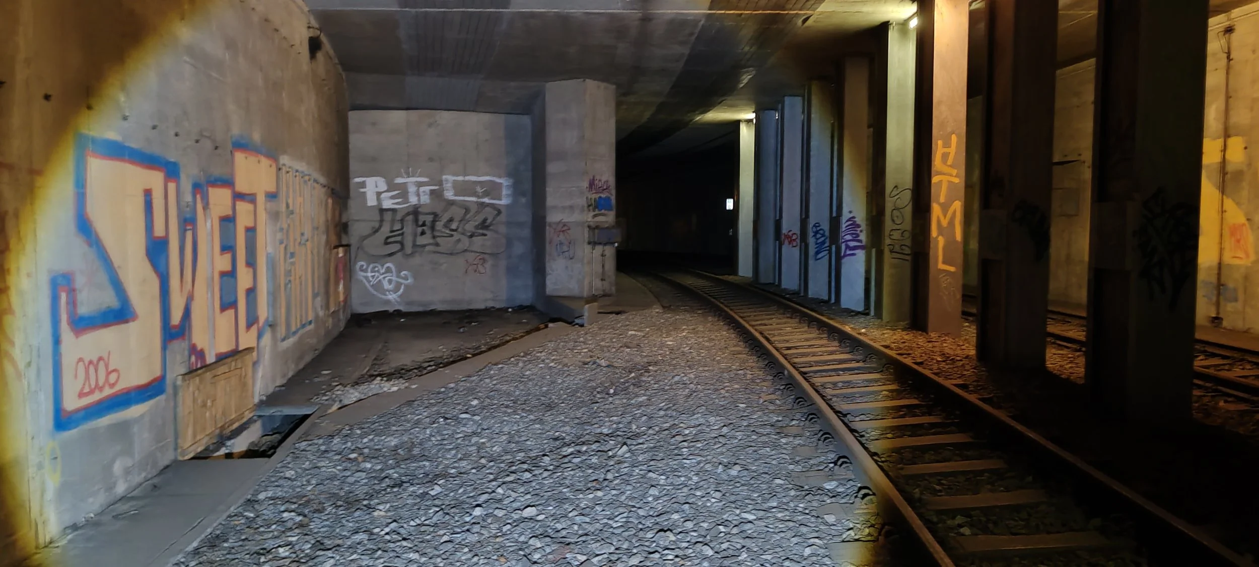 Ein Eisenbahntunnel mit Graffiti an den Wänden und Schienen auf dem Boden.