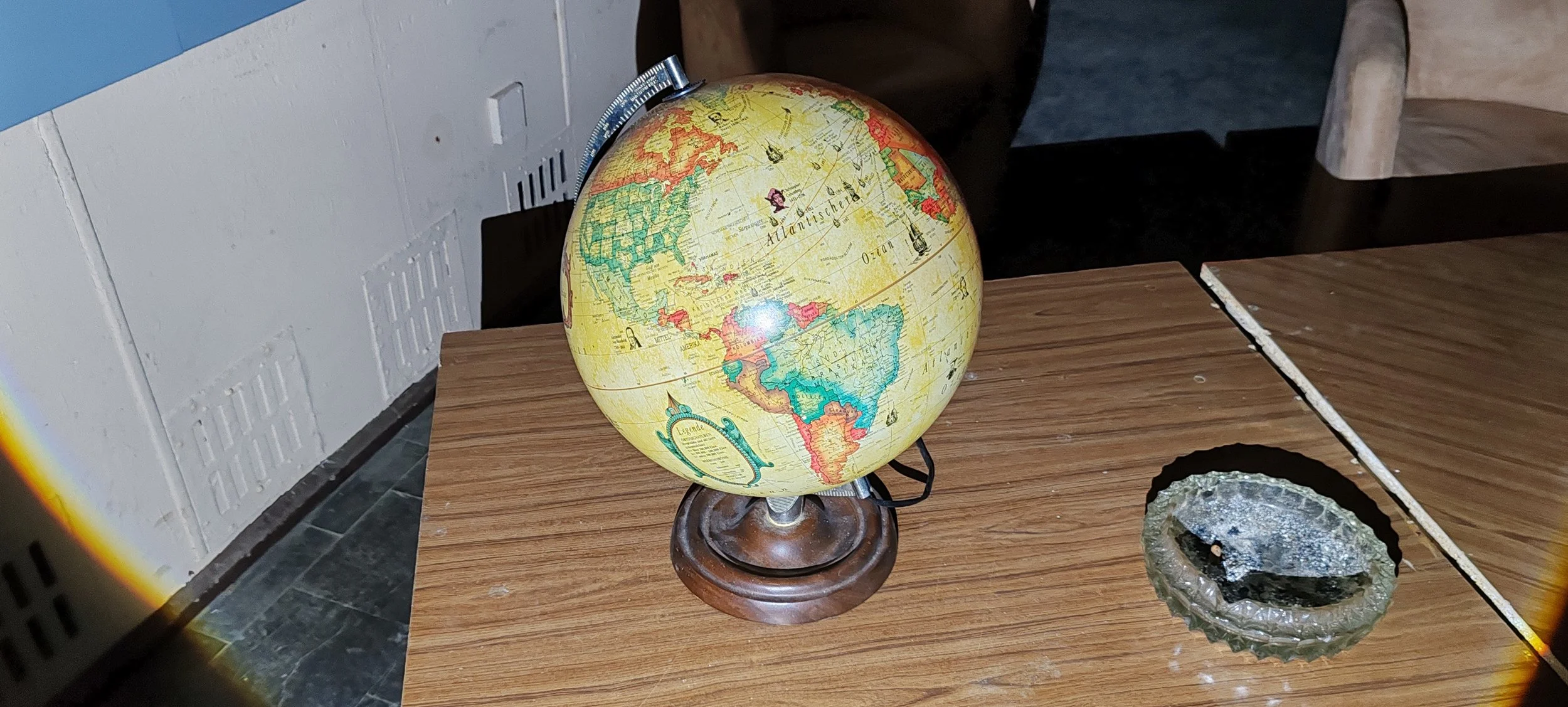 Ein Globus auf einem Holzschreibtisch neben einer gläsernen Aschetonne.