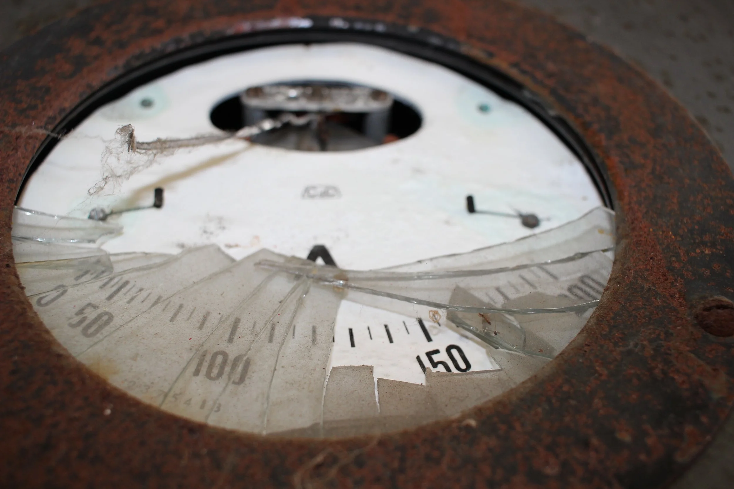 Ein zerbrochenes, verrostetes Zifferblatt einer Uhr mit zerbrochener Glasscheibe.