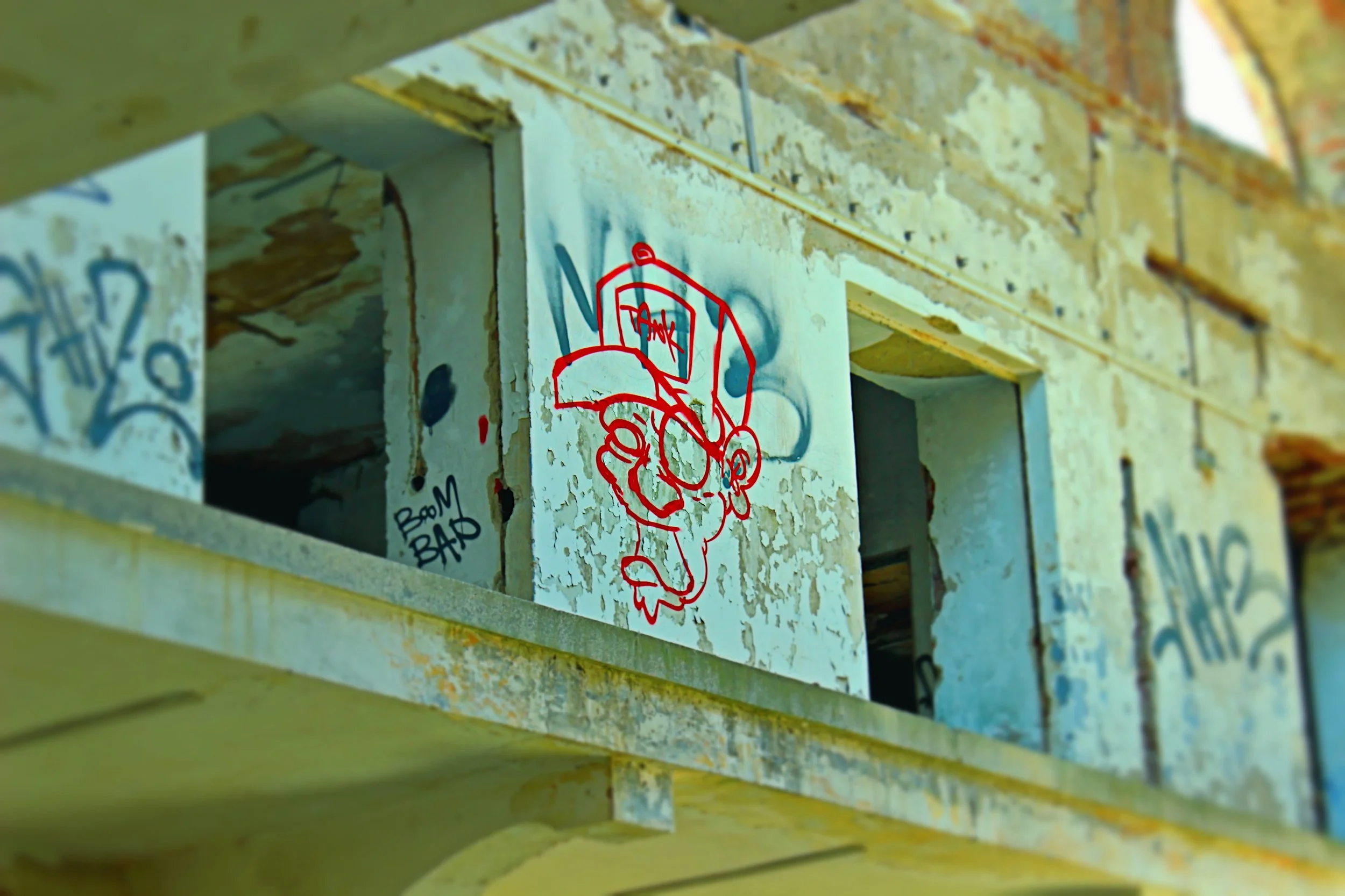 Graffiti eines roten Cartoon-Charakters mit Brille und Cappuccino auf einer alten, verfallenen Gebäudewand.