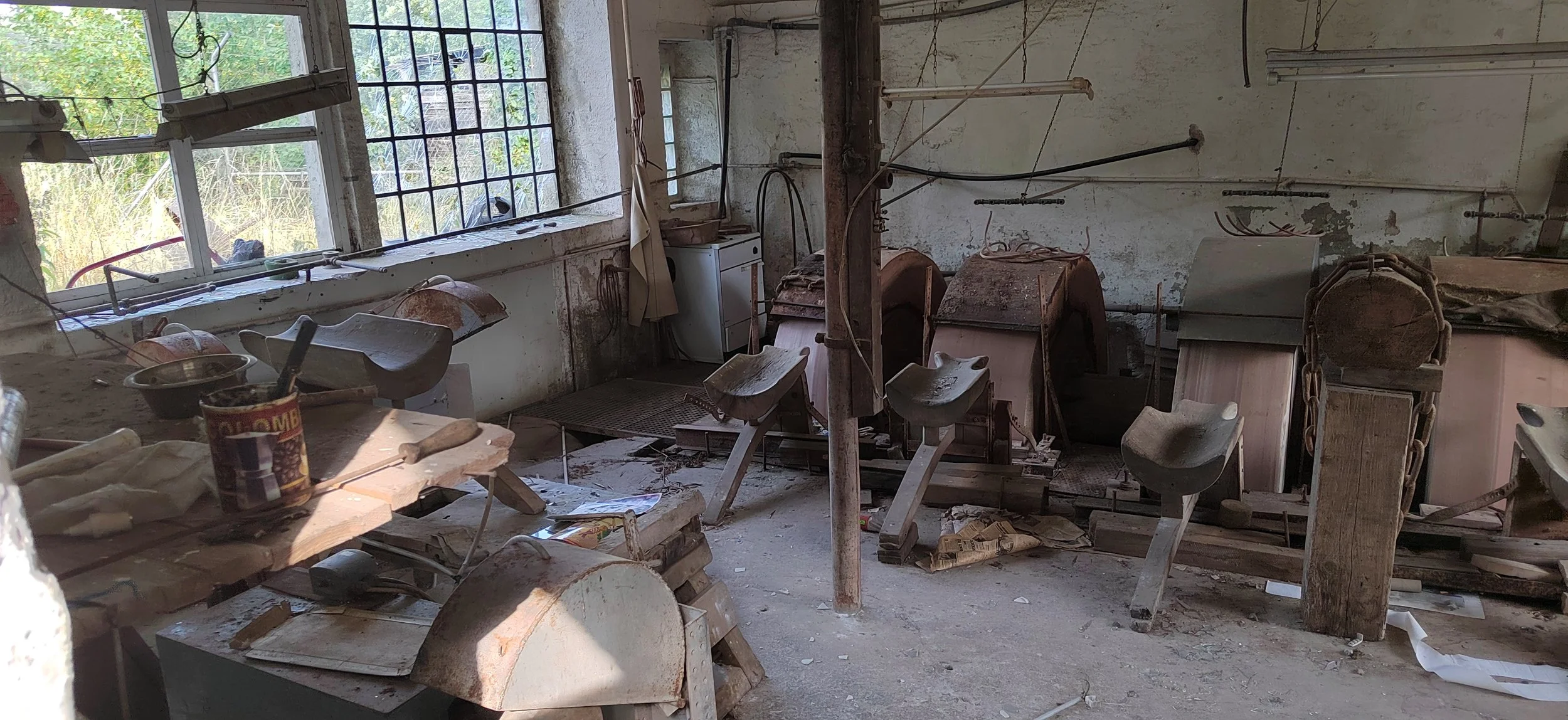 Ein verlassener handwerklicher Raum mit alten Maschinen und Werkzeugen, Staub und Unordnung, durch Fenster wird natürliches Licht hereingelassen.