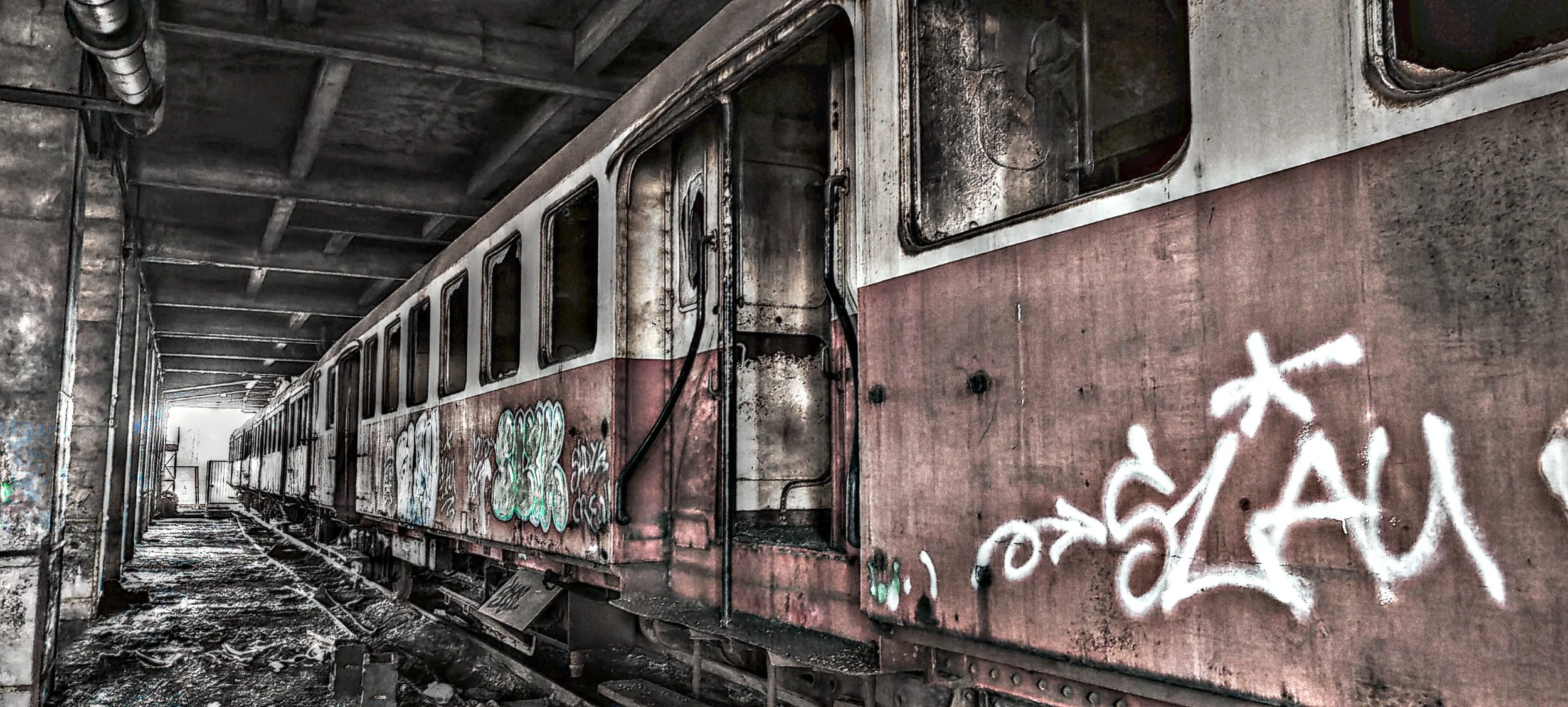 Verlassener und verrosteter Zug in einer alten Eisenbahnhalle, beklebt mit Graffiti.