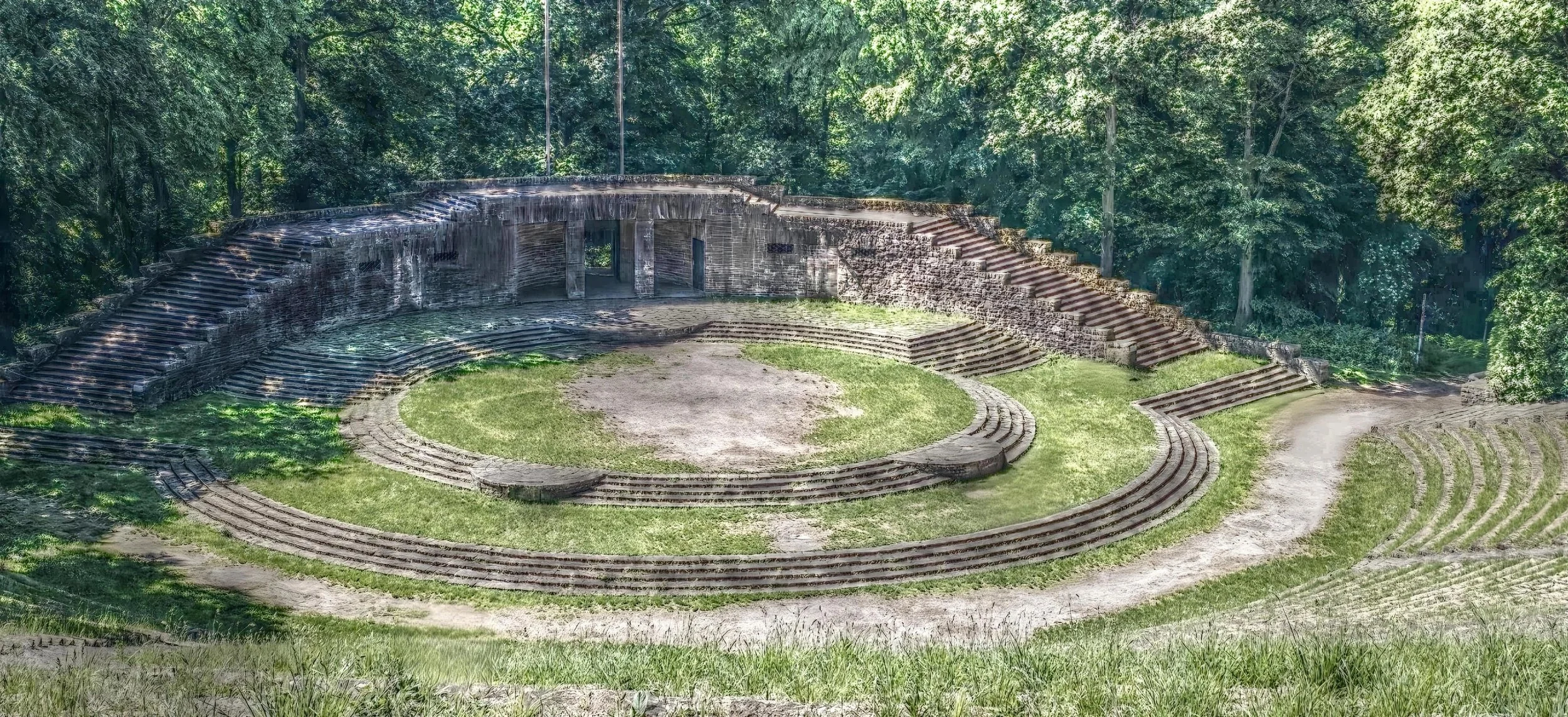 Antikes römisches Amphitheater im Grünen, umgeben von Bäumen.