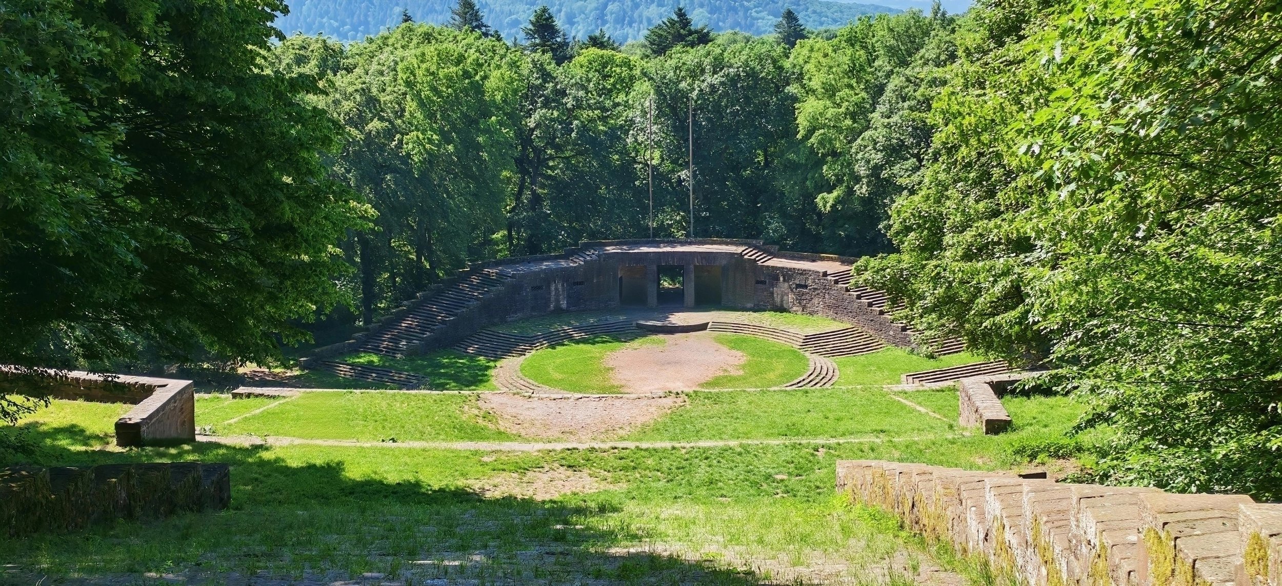 Römisches Theater im Grünen, umgeben von Bäumen, mit Stufen und alten Mauern.