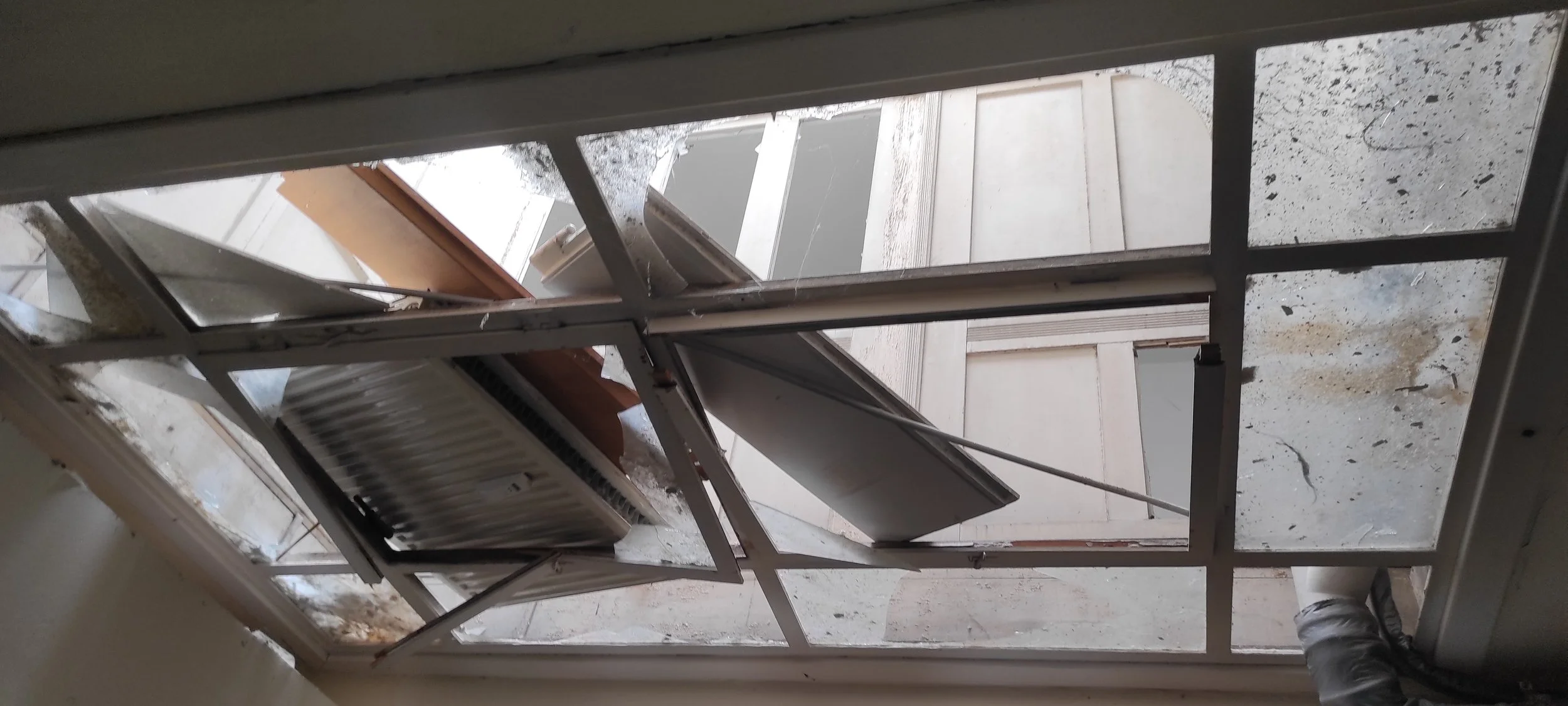 Kaputte Fenster und teilweise zerstörter Balkon, voller Schutt und Staub.
