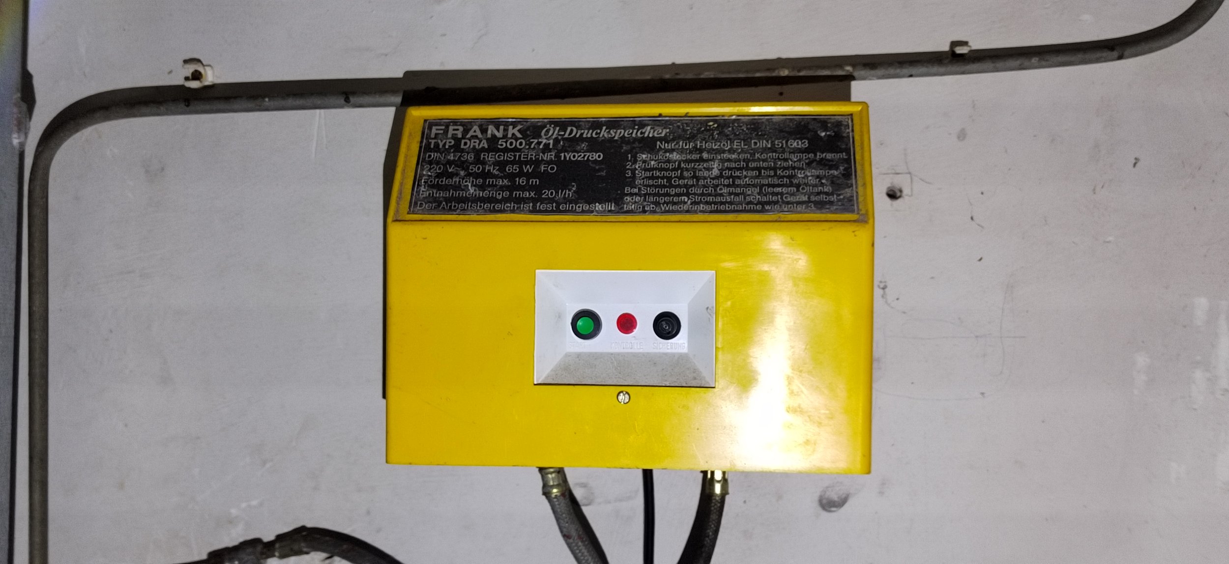 Gelbe Öldruckspeicher mit Steuerung und Kontrollleuchten, an einer Wand montiert.