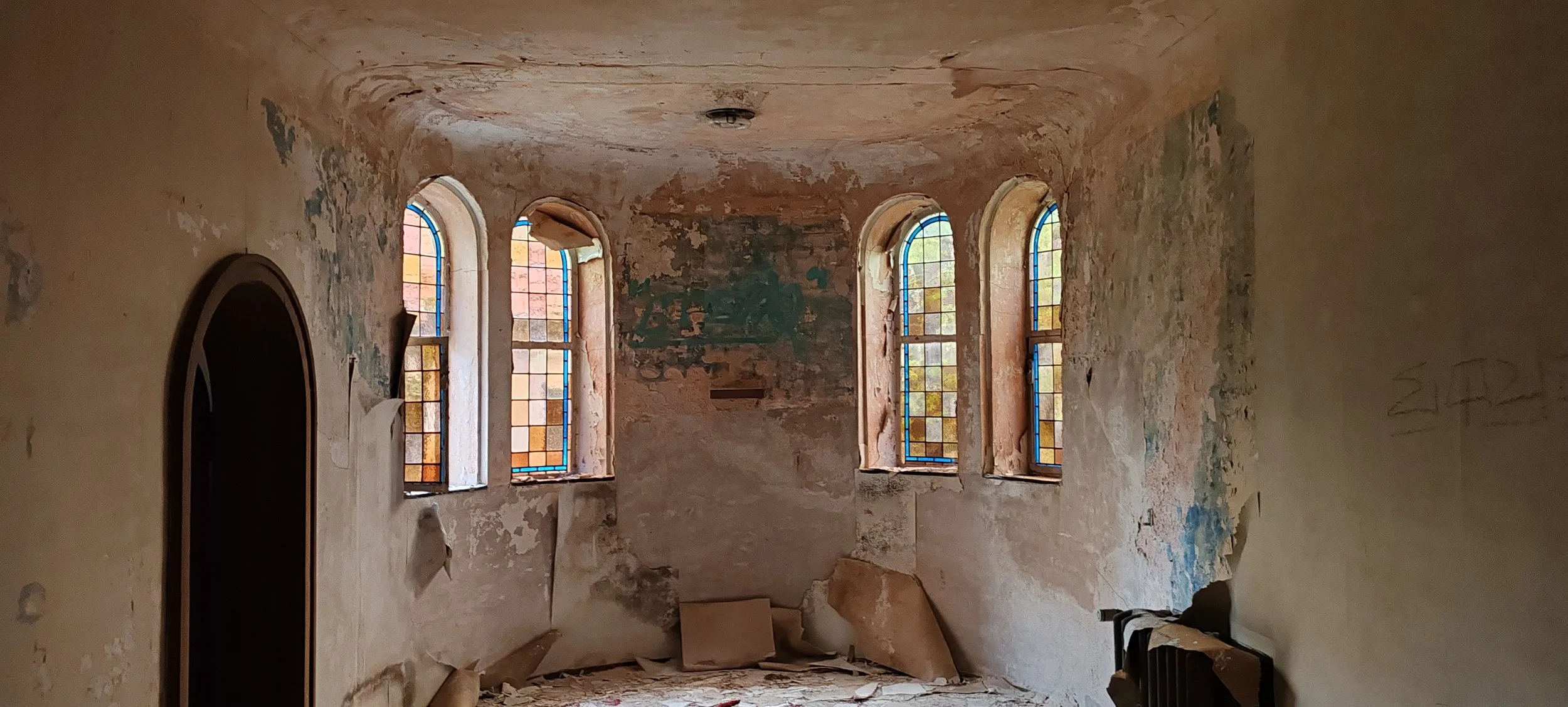 Alte, verfallene Kirche mit bunten, zerbrochenen Fenstern und abblätternder Wandfarbe.