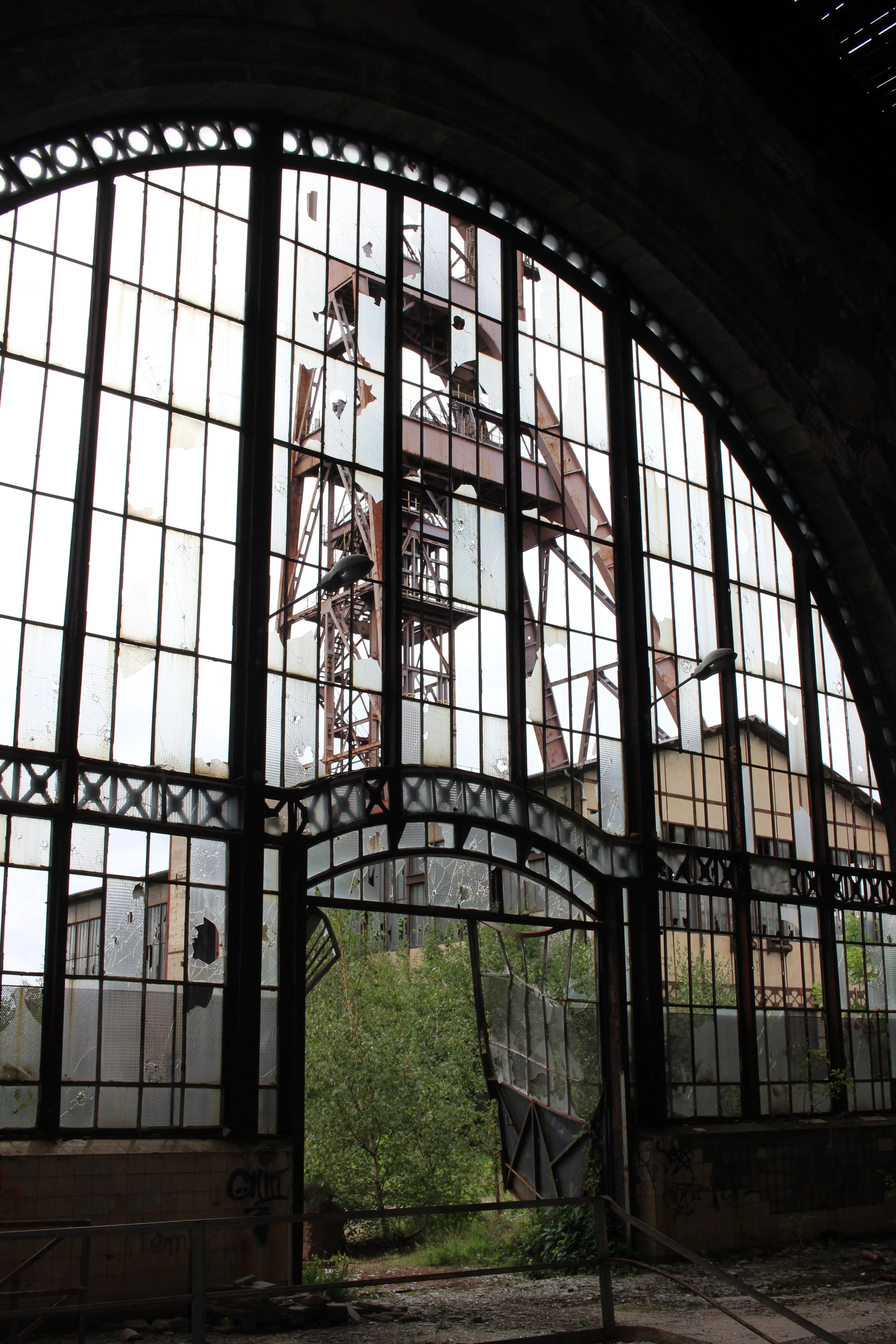 Ein verfallenes Gebäude mit zerbrochenen Fenstern, durch das eine verrostete Industriemaschine zu sehen ist.