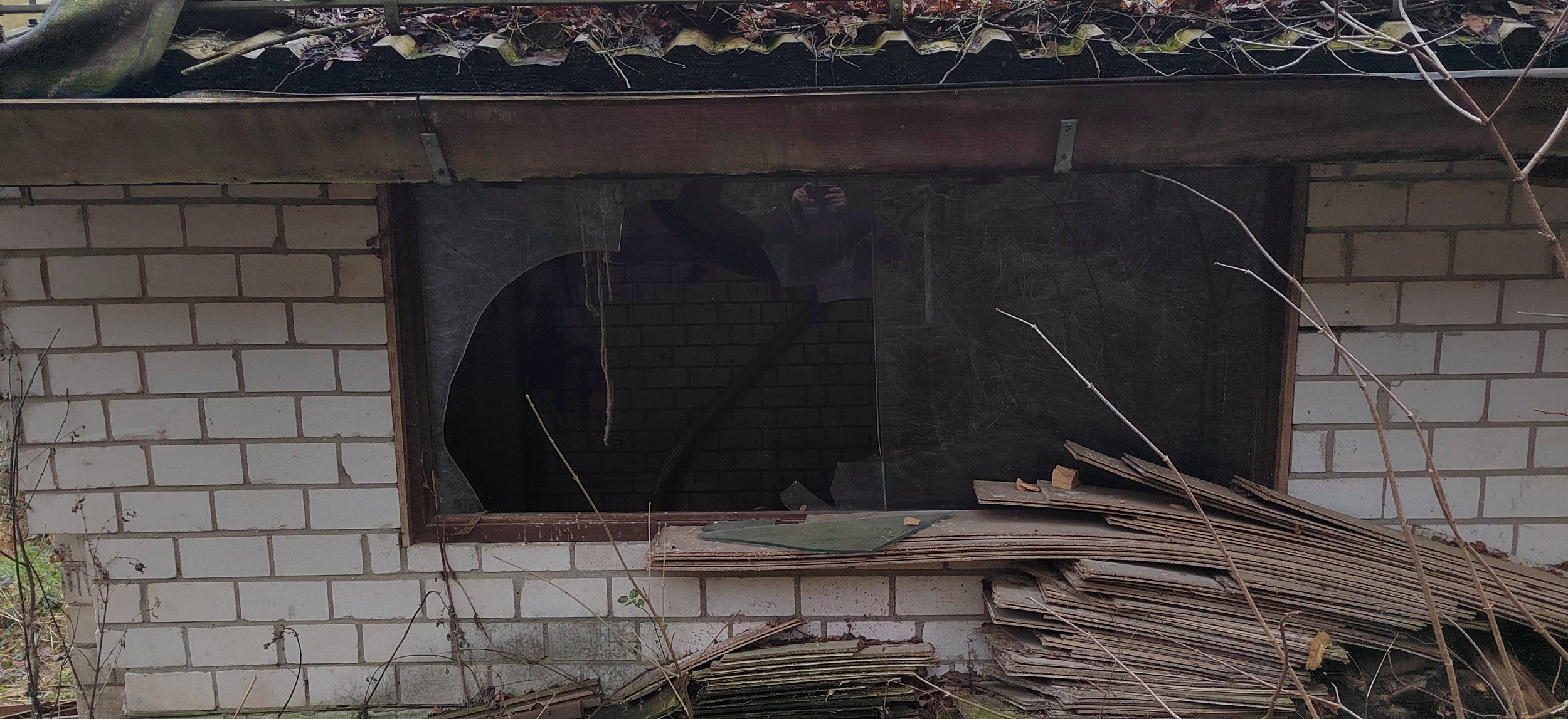Ein verfallenes Gebäude mit einem zerstörten Fenster und abgelegtem Holz vor der Wand.