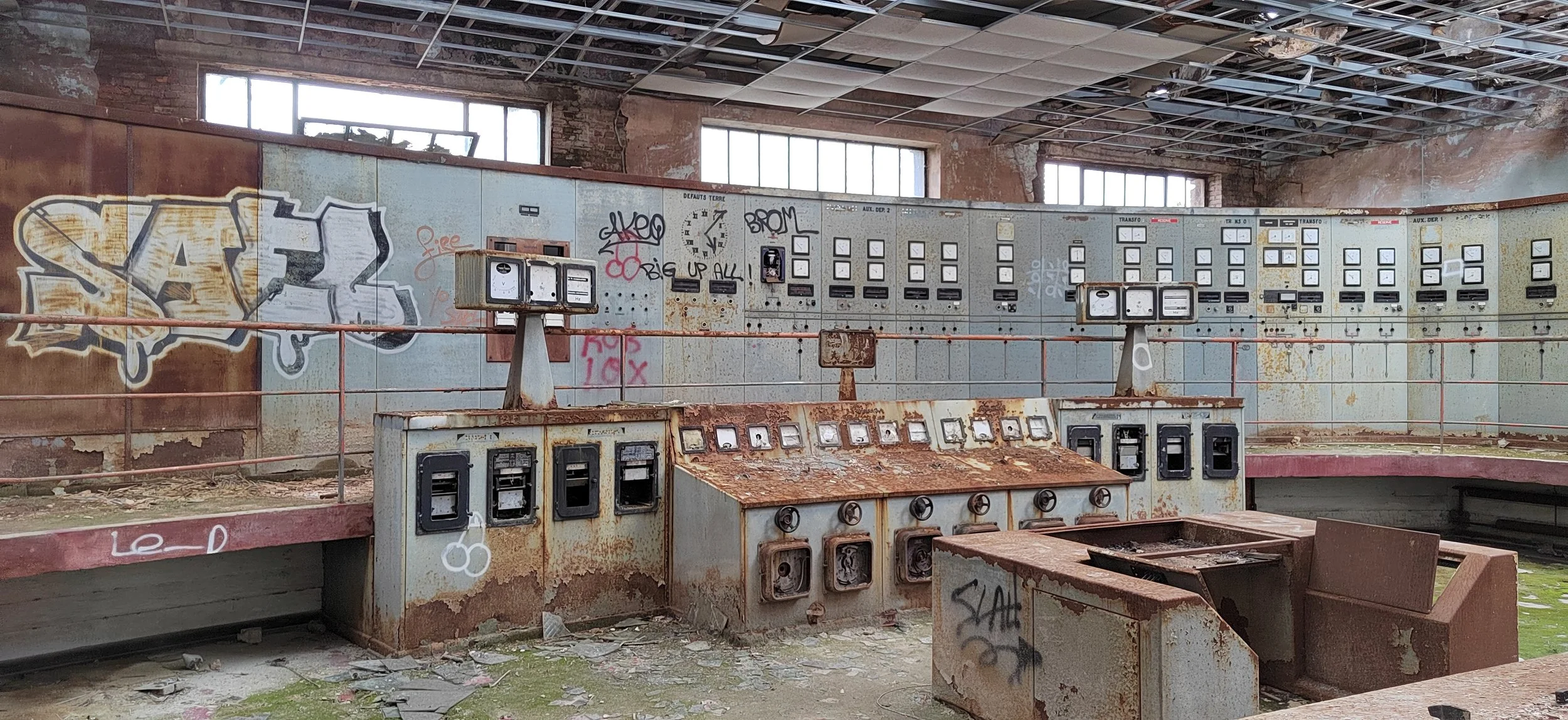 Veraltete, verrostete und beschädigte Steuerkontrolltafel in einem verlassenen Industriegebäude mit Graffiti an den Wänden.