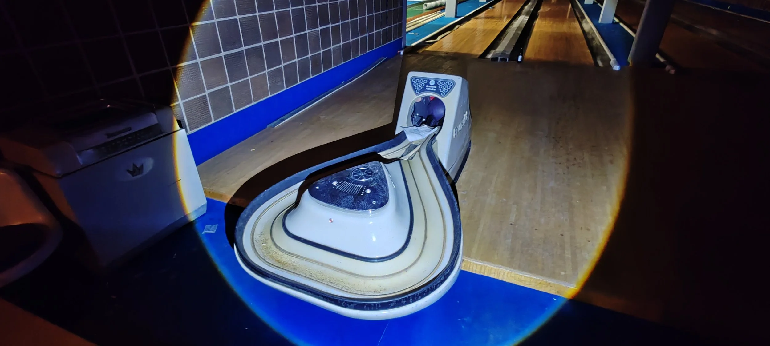 Ein automatischer Bowling-Automat auf einer Bowlingbahn in dunkler Umgebung, beleuchtet durch eine Taschenlampe.