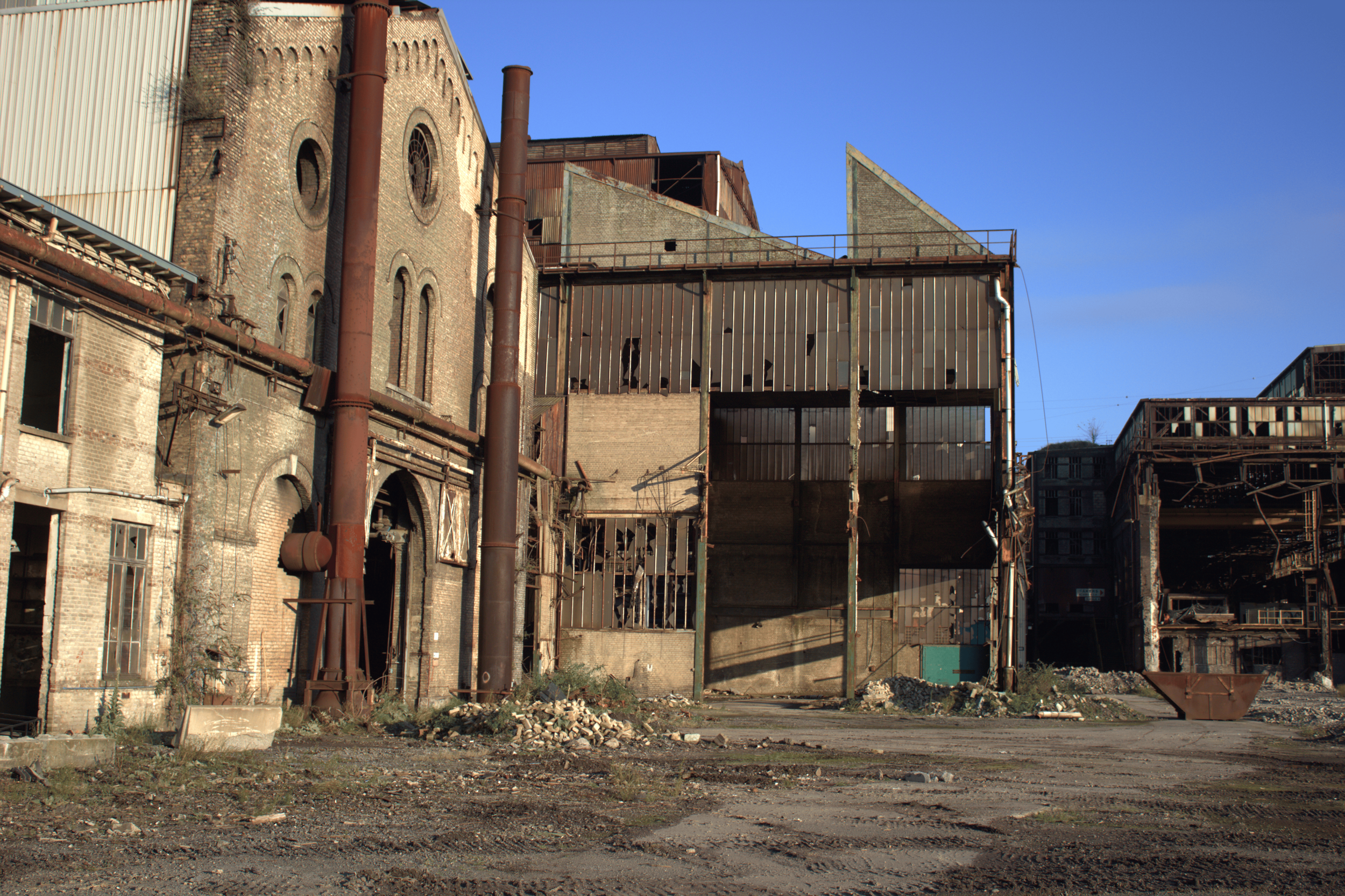 Verlassene, zerstörte Industriehalle mit rostigen Wänden und Papieren, trübe Stimmung, grelle Schatten, alles in braun- und grautönen, blauer Himmel