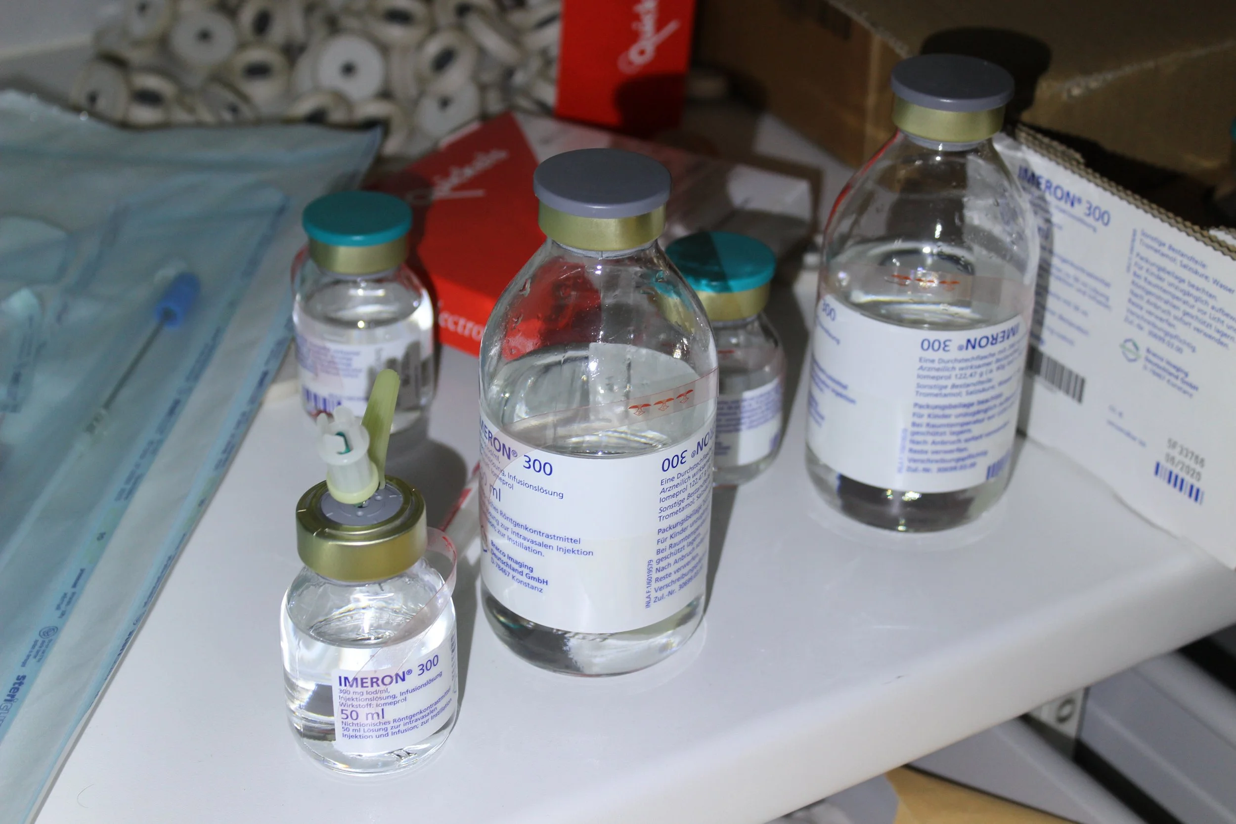 Mehrere Flaschen mit Medikamenten, darunter Impfstoff, auf einem medizinischen Tisch, umgeben von medizinischem Zubehör.