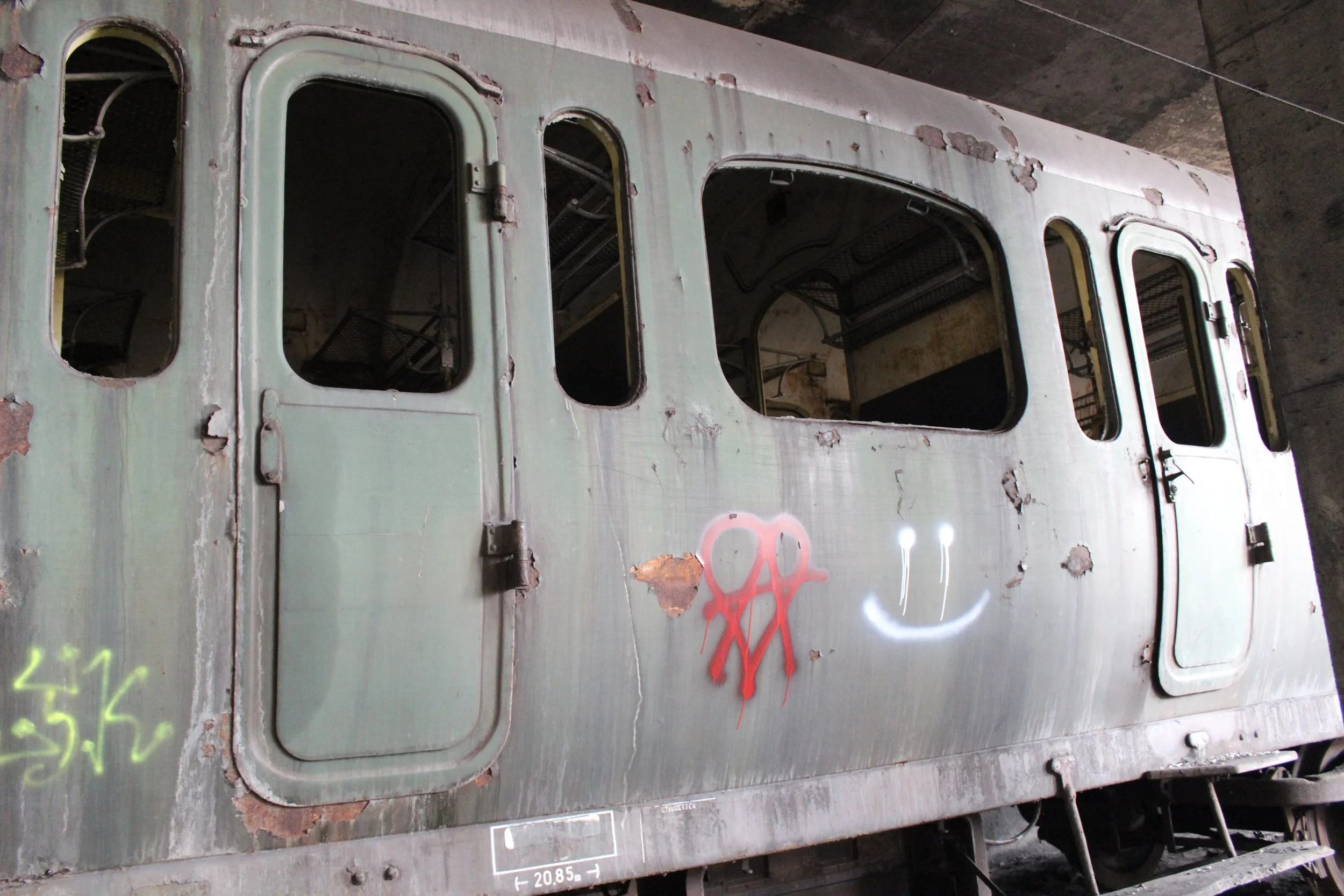 Ein alter, verrosteter Eisenbahnwagen mit graffiti auf der Seite, darunter eine lachende Smileygrafik und eine rote Zeichnung