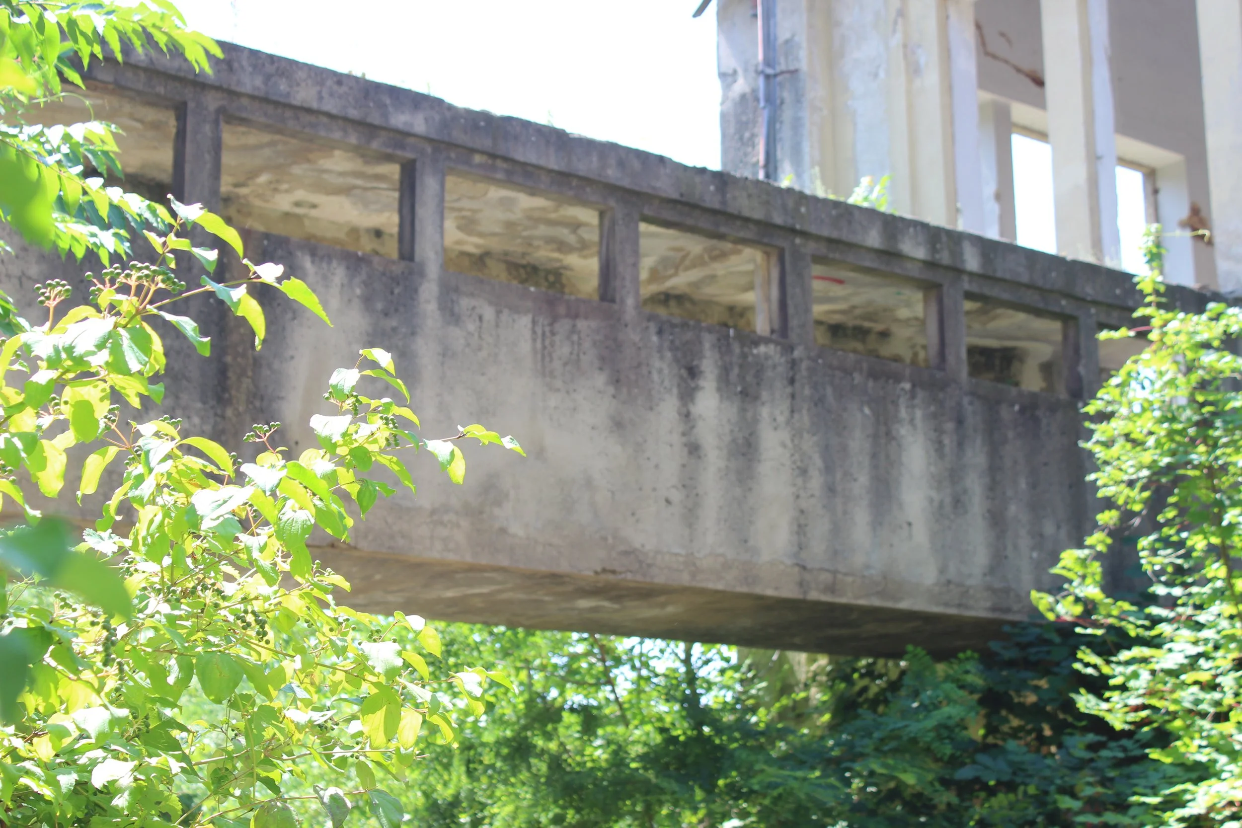 Ein unvollendetes Gebäude mit einer Betonbrücke darüber, umgeben von grünen Bäumen.