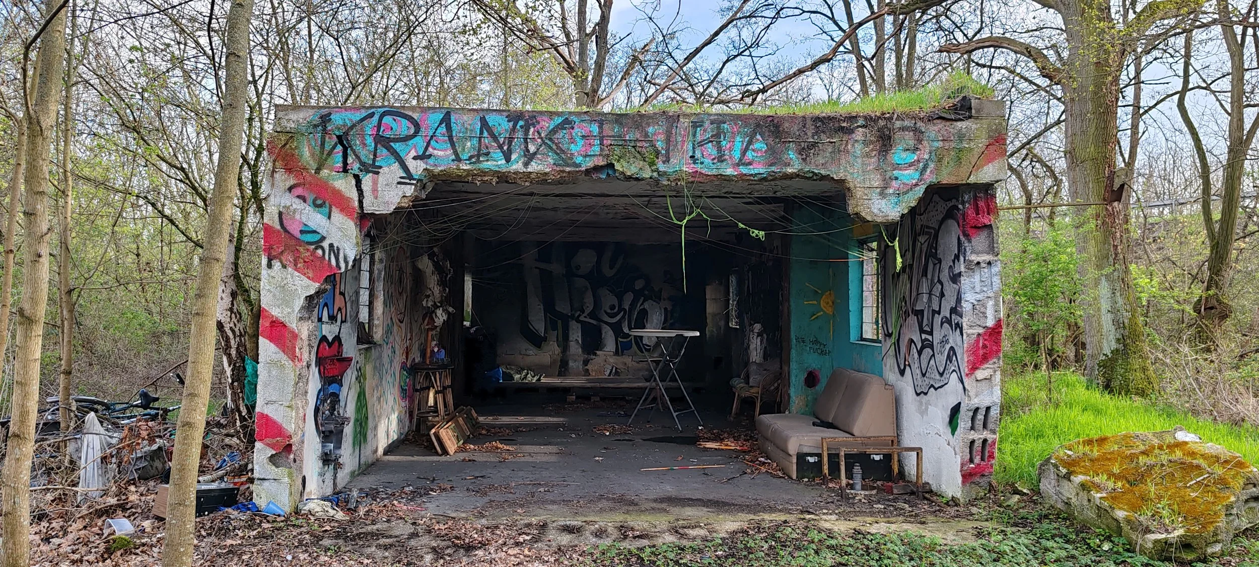 Verfallene, graffiti- bedeckte Garage in einem Waldgebiet mit altem Sofa und Müll vor der Tür.