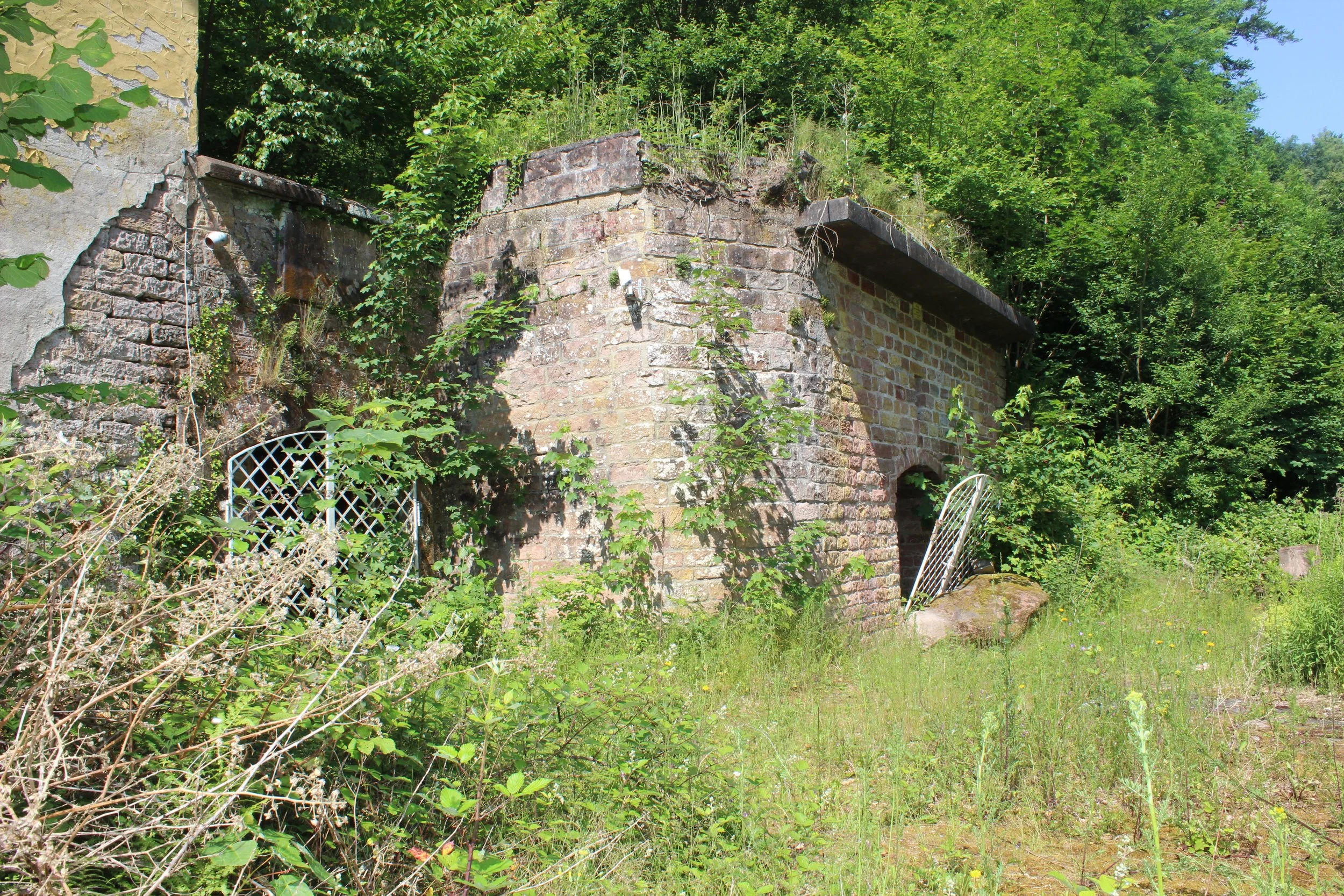 Verfallene alte Steinbrücke im Grünen, umgeben von Pflanzen und Bäumen.