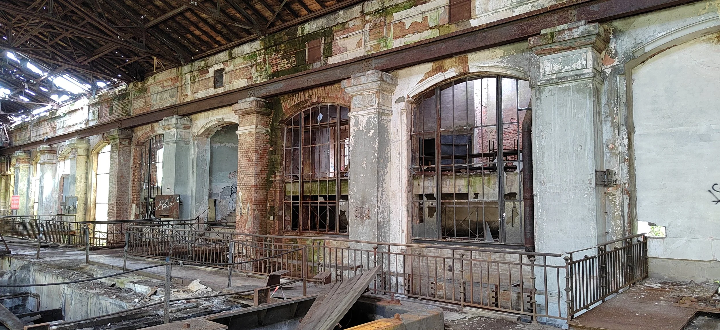 Verlassene, alte Fabrikhalle mit zerbrochenen Fenstern, rostigem Metall, abblätternder Farbe und Graffiti auf den Wänden.